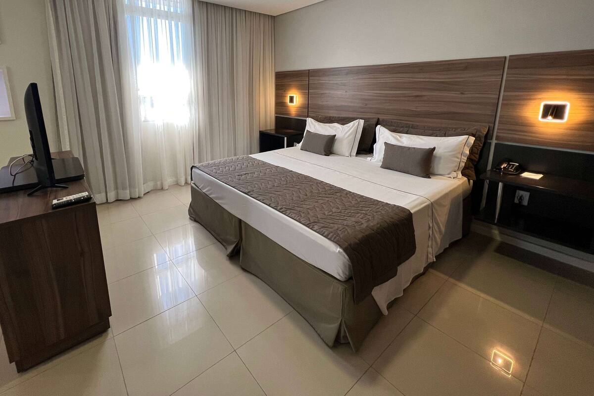 Quarto de hotel moderno com uma cama grande, uma escrivaninha e um computador.