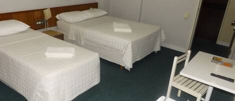 A hotel room with two single beds, a small table with a remote control, and a chair.