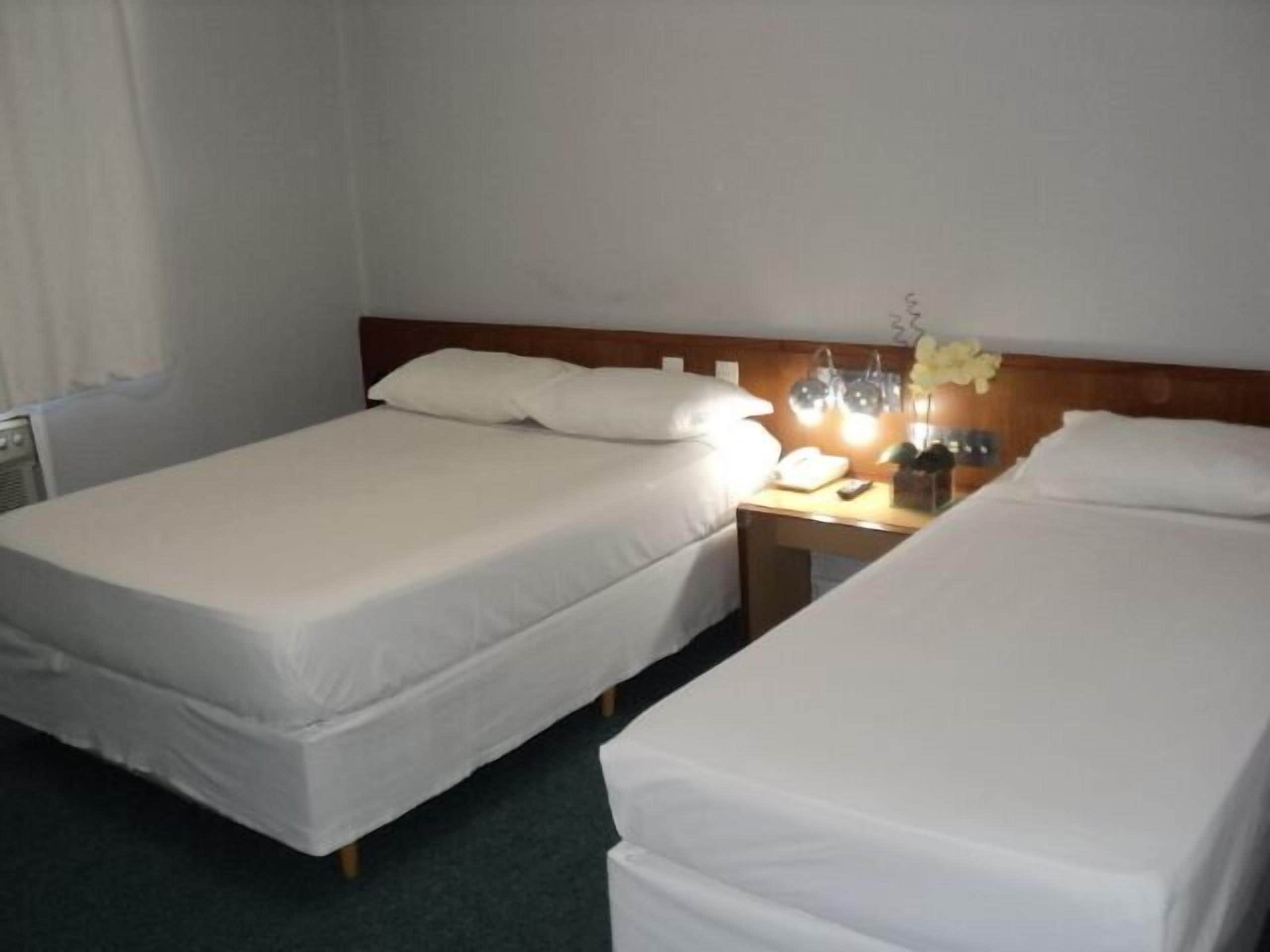 Une chambre d’hôtel avec deux lits simples, une table de chevet avec une lampe, un téléphone et un petit vase avec des fleurs.