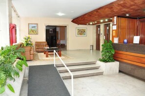 A reception area with a reception desk, a sofa, a coffee table, and a staircase leading to an upper floor. - Rede Andrade San Martin (Curitiba)