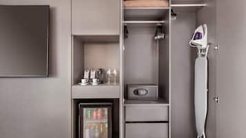 A hotel room with a minibar, a refrigerator, a safe, a hanging iron, and a coat rack.