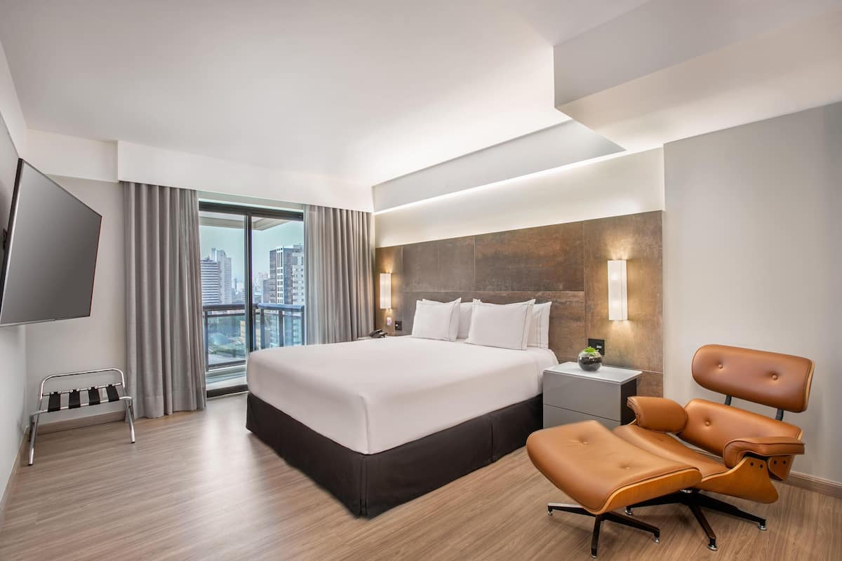Quarto de hotel moderno com cama grande, área de estar, televisão e vista para a cidade.