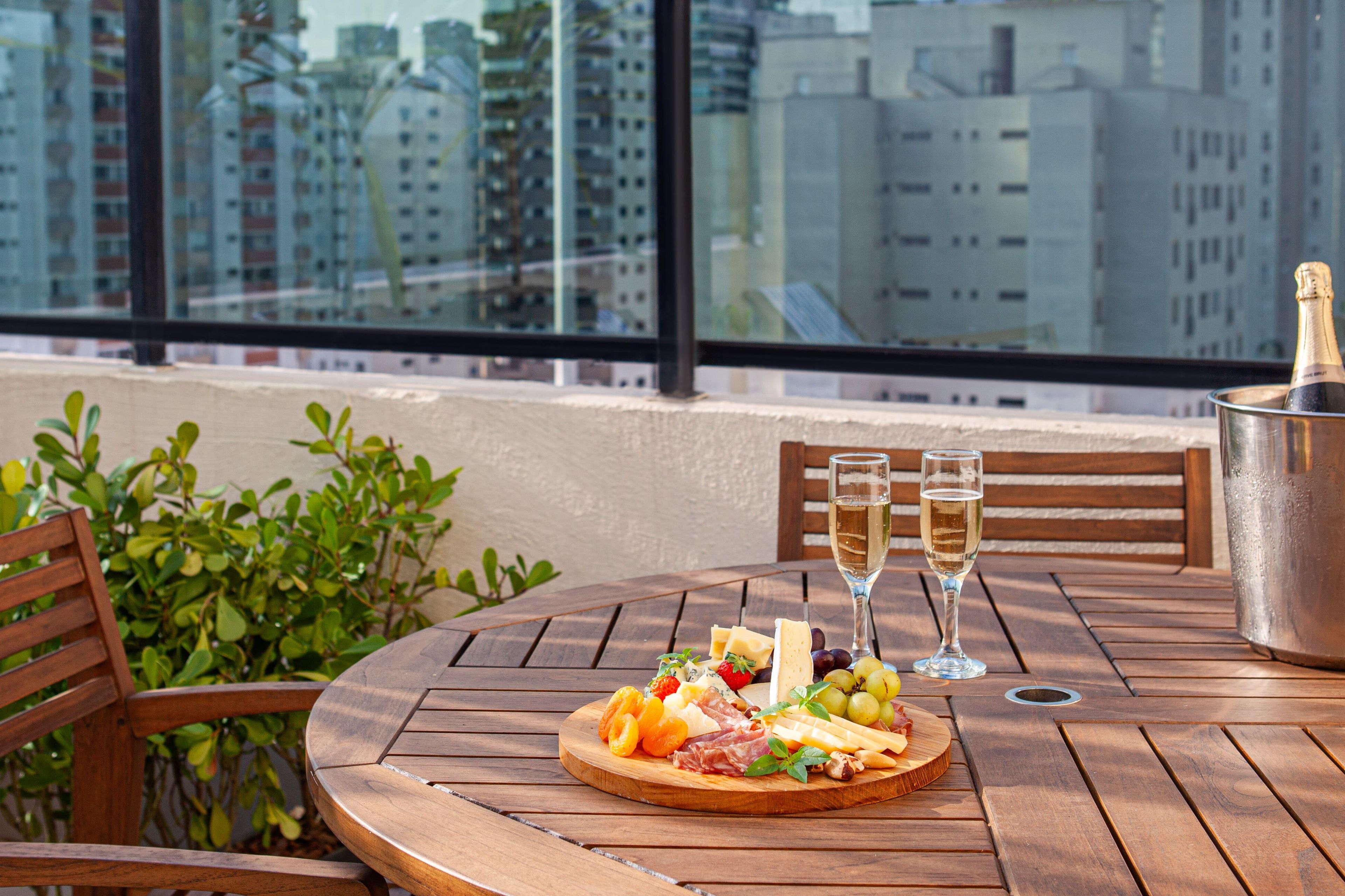 Uma mesa de madeira com uma tábua de frios, dois copos de champanhe e uma garrafa de champanhe em um balde de metal.