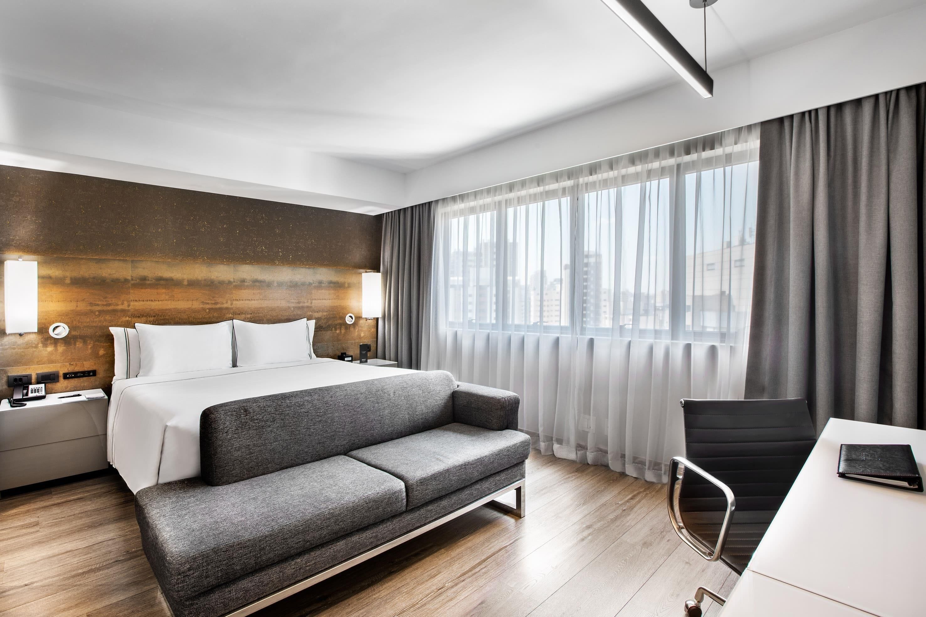 A modern hotel room with a large bed, a sofa, a desk, and a chair.