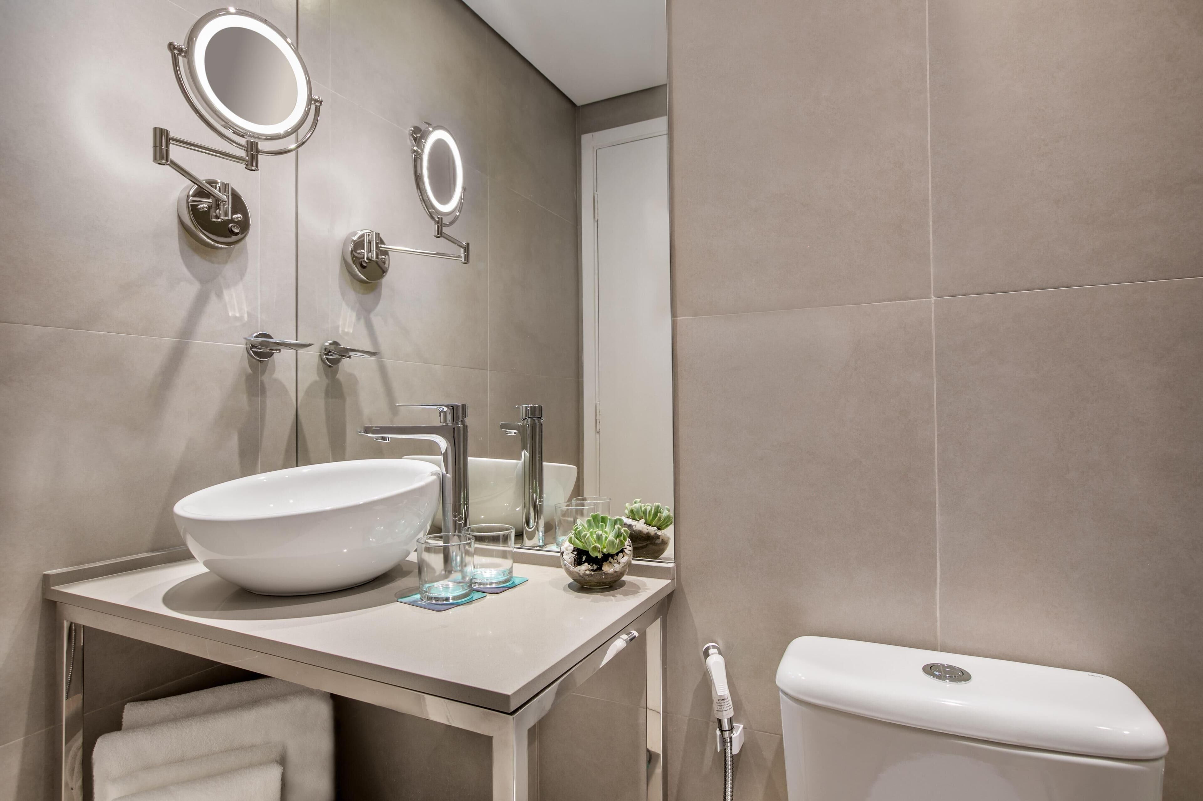 A modern bathroom with a large sink, two mirrors, a toilet, and a towel rack.