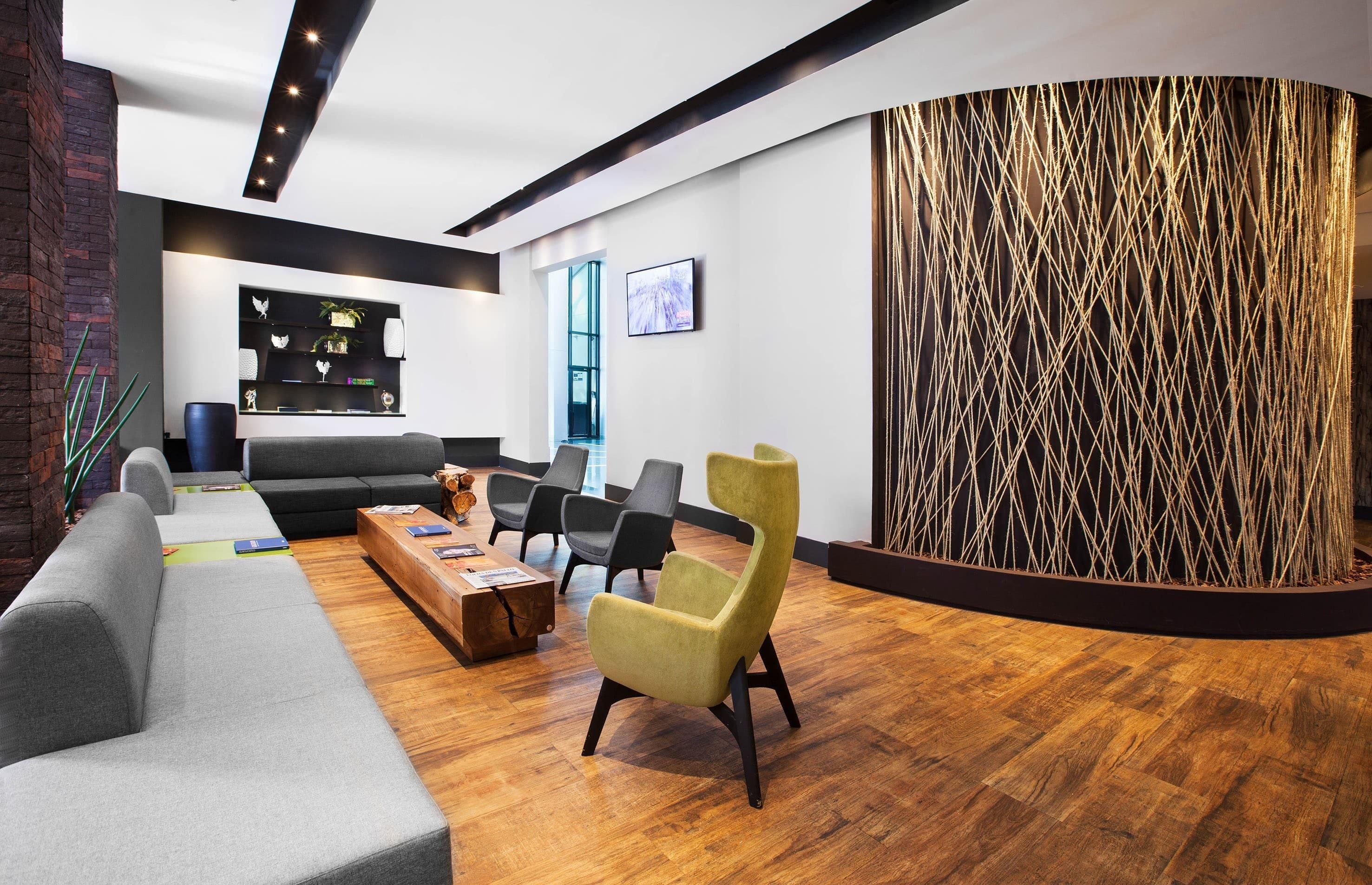 A modern lobby with a grey sofa, black chairs, a wooden coffee table, and a unique textured wall.