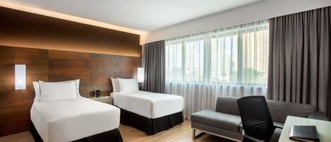 A hotel room with two beds, a sofa, a desk, and a large window with curtains.