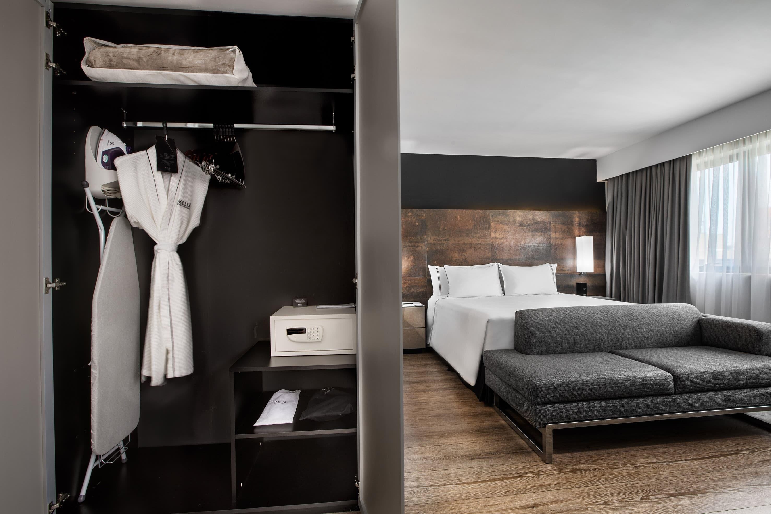 Una habitación de hotel moderna con una cama, un sofá gris, un armario y una mesita de noche.