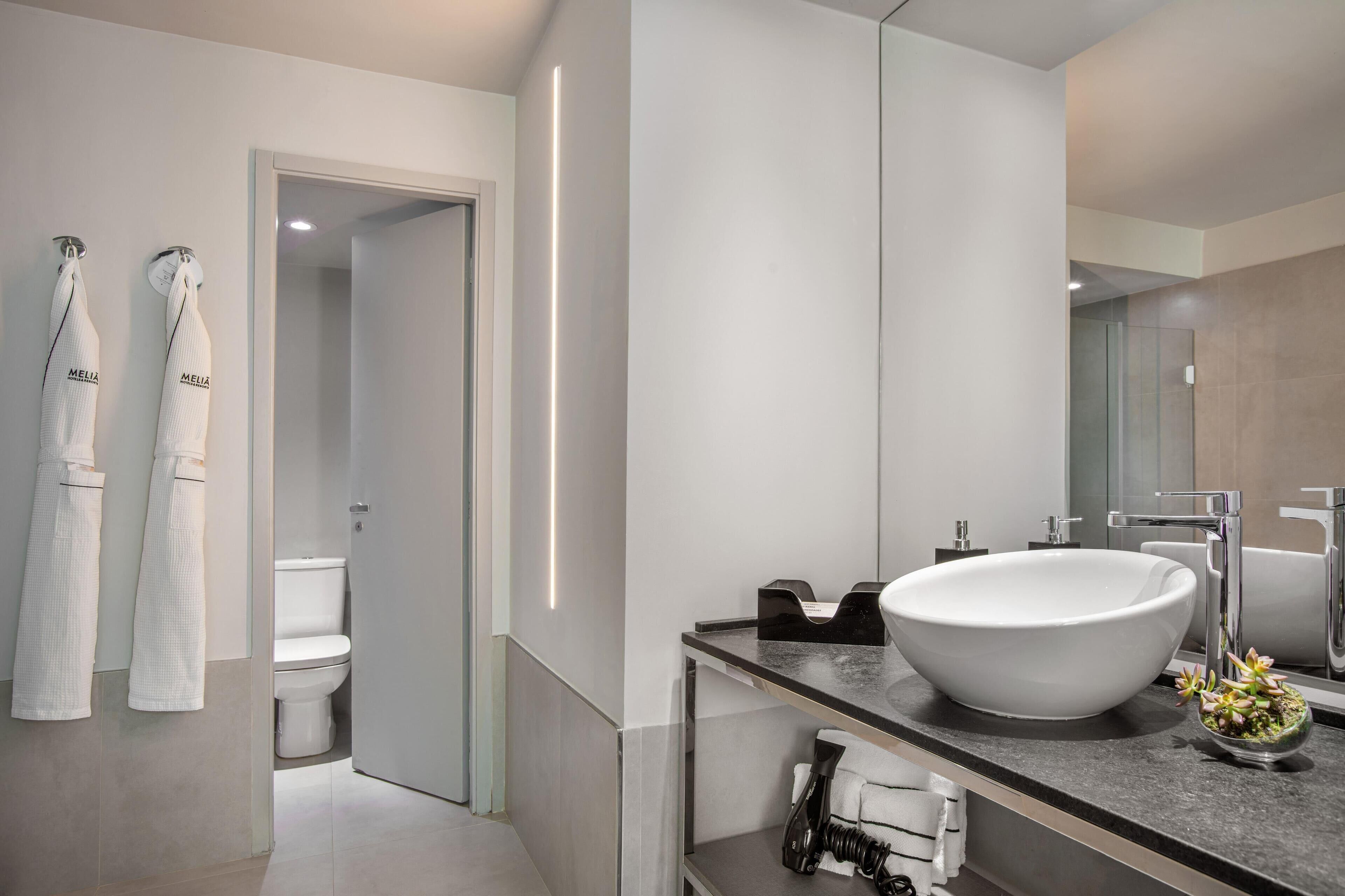 Un baño moderno con un lavamanos grande de color blanco, un espejo y dos toallas colgadas en ganchos.