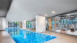 Una piscina interior con un diseño azul a cuadros, rodeada de equipamiento de gimnasia y grandes ventanales.