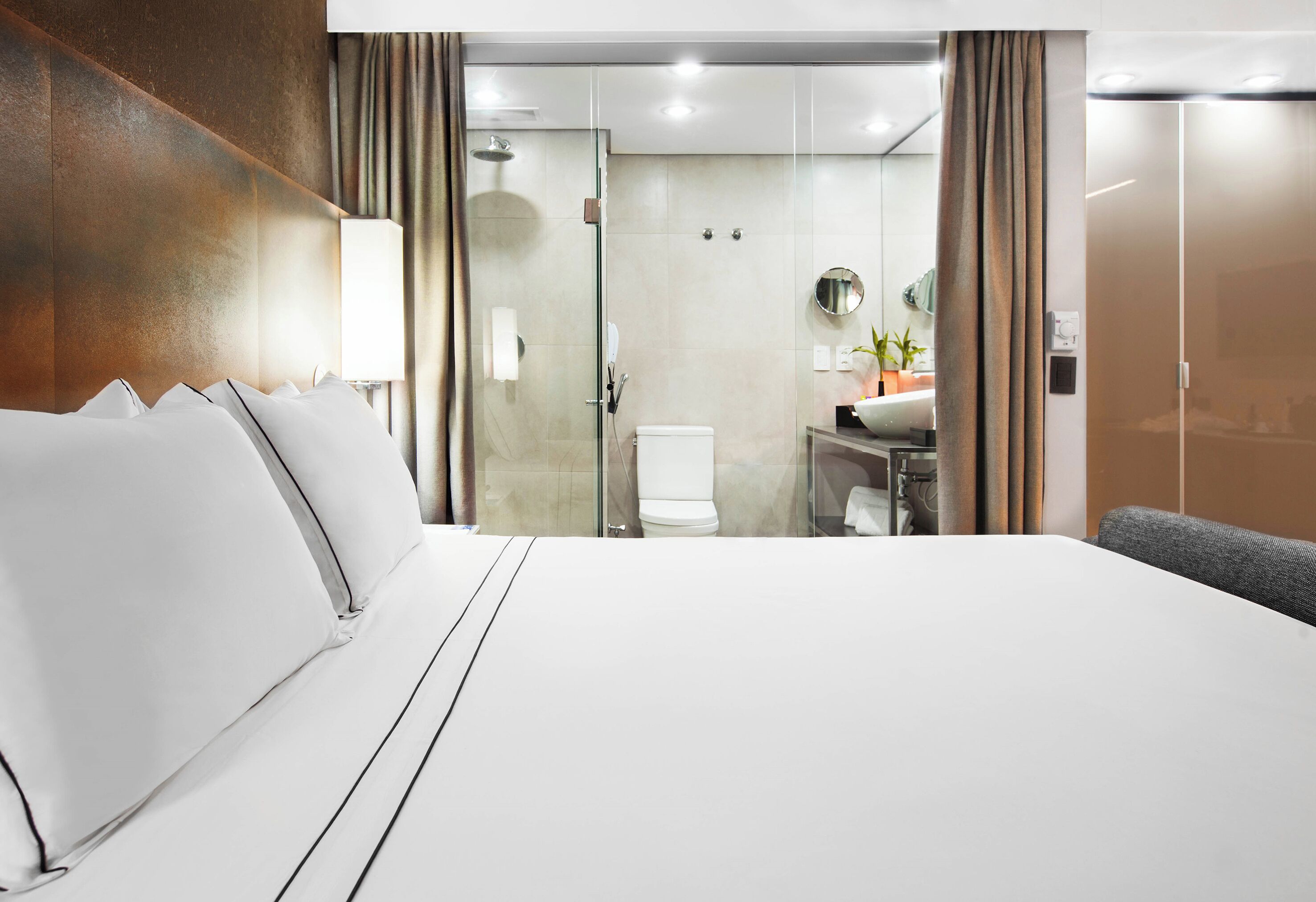 Habitación de hotel con una cama grande, cabina de ducha de vidrio, baño con inodoro y lavamanos.