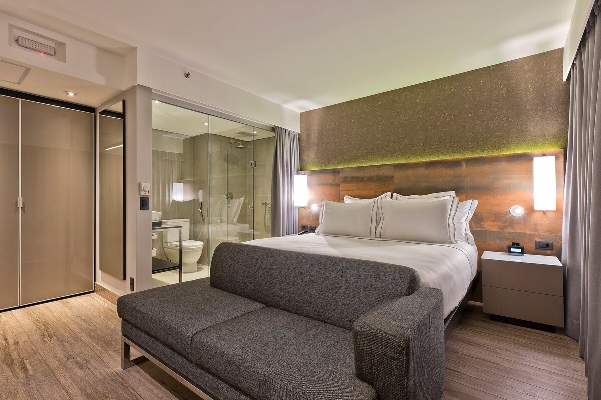 Una habitación de hotel moderna con cama, mesita de noche y zona de estar.