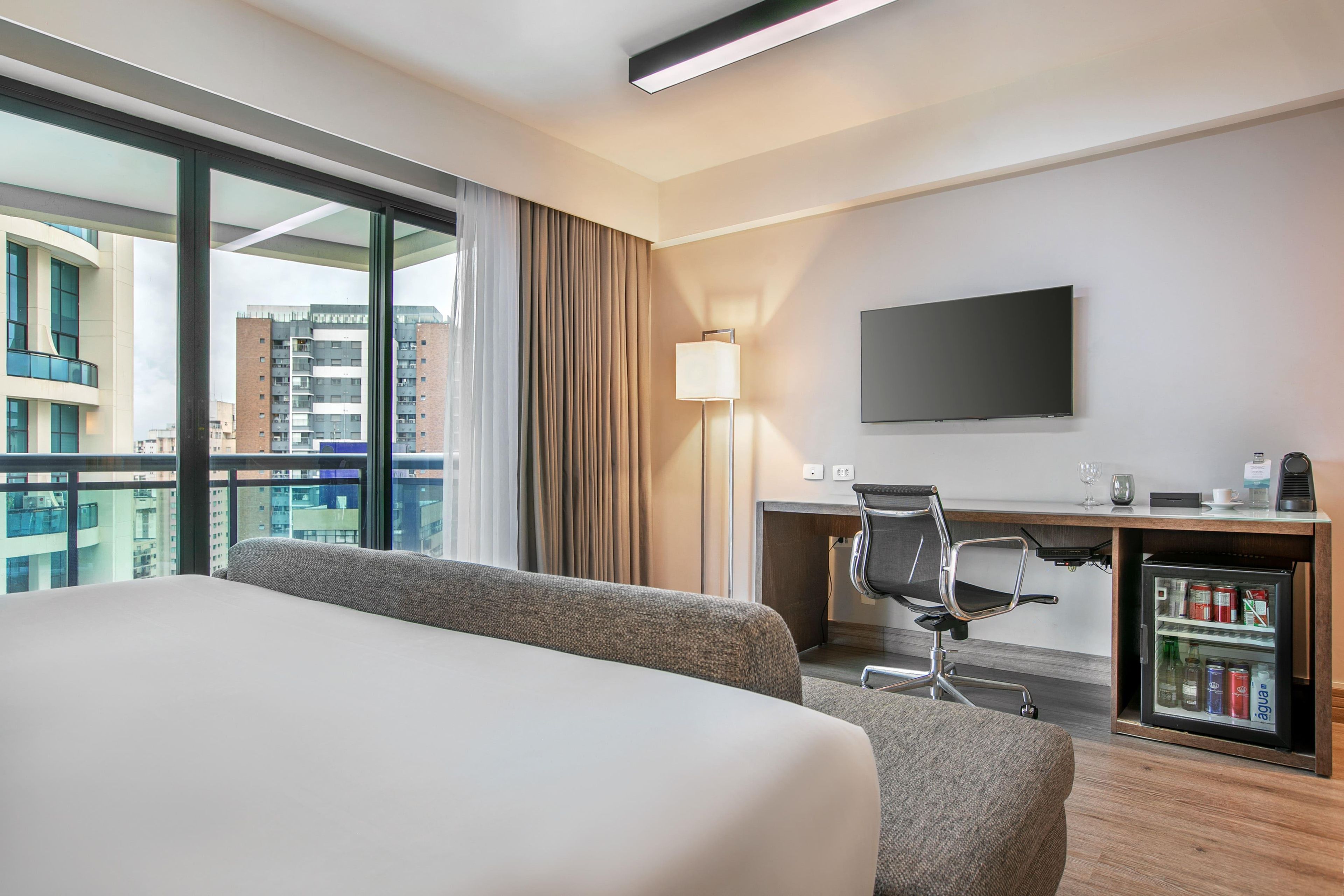 Una habitación de hotel con cama, escritorio, silla, televisor y minibar.