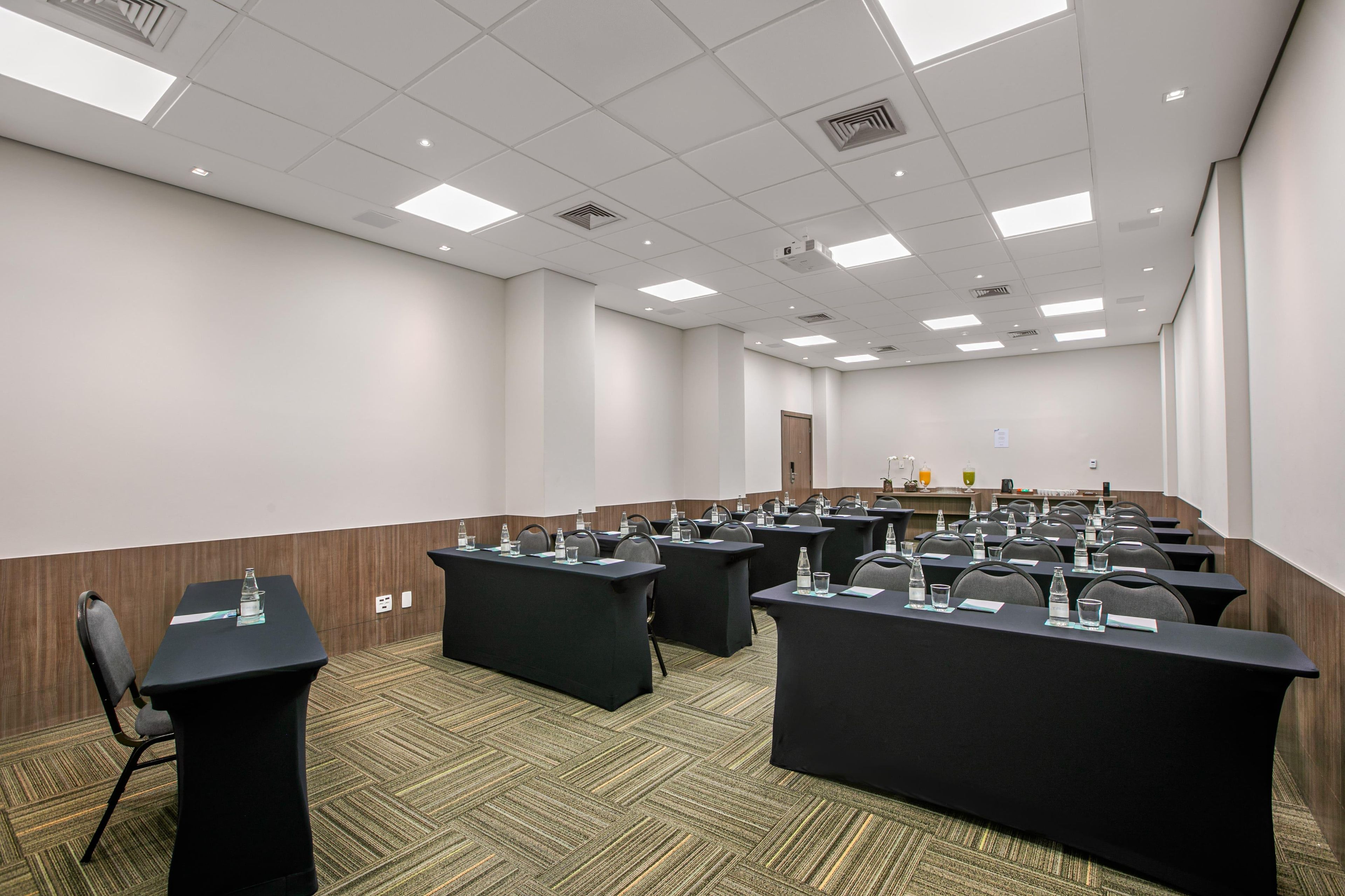 Uma sala de conferências com várias mesas, cadeiras e uma tela de projeção.