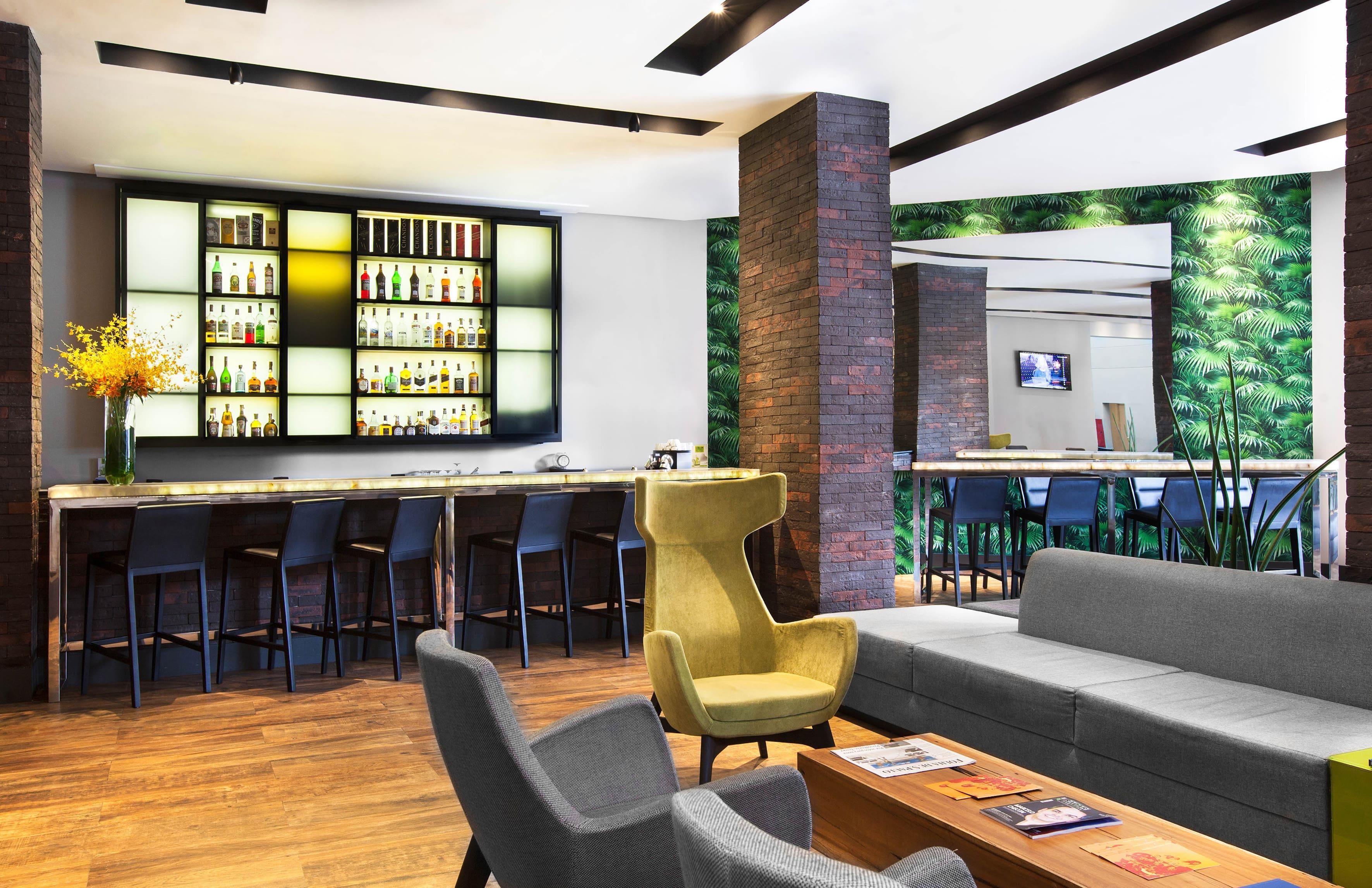 Eine moderne Bar mit einer Auswahl an Spirituosenflaschen, einer Sitzecke mit Sofa und Sesseln sowie einer Wandverkleidung mit einer Ziegelsteinsäule.
