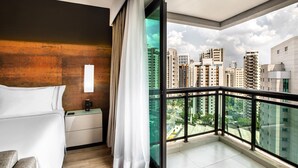 Una habitación de hotel moderna con balcón, cama, mesita de noche y vista a la ciudad.