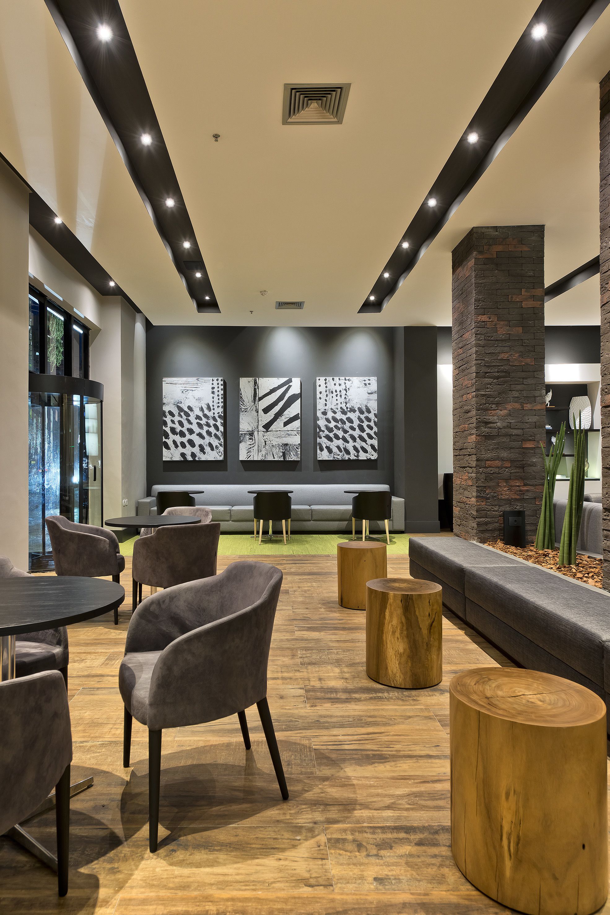 Un espace détente moderne avec des fauteuils gris à revêtement en tissu, des tables rondes en bois et un canapé gris.