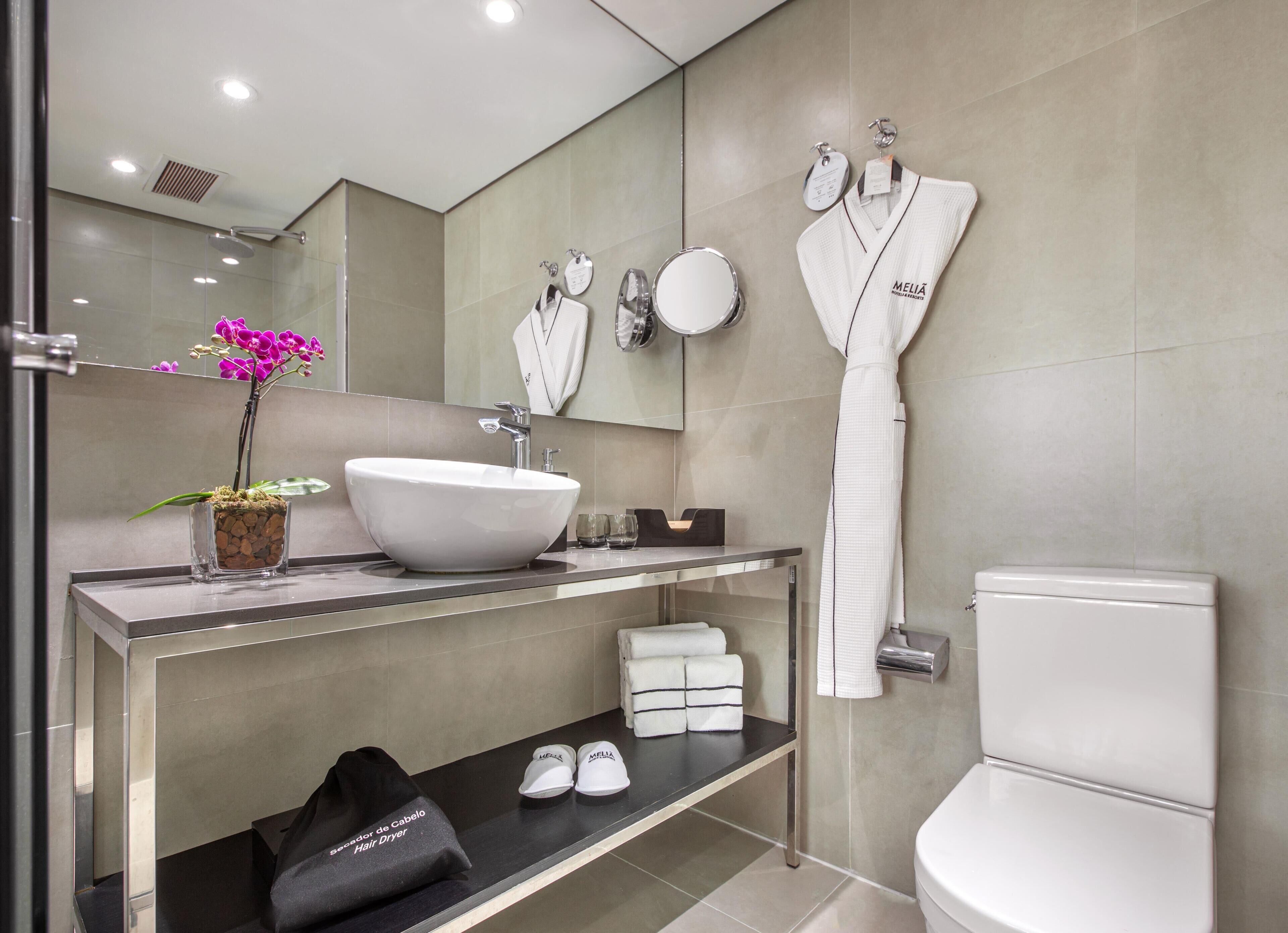 Un baño moderno con un lavamanos blanco grande, un espejo, un perchero y un inodoro.