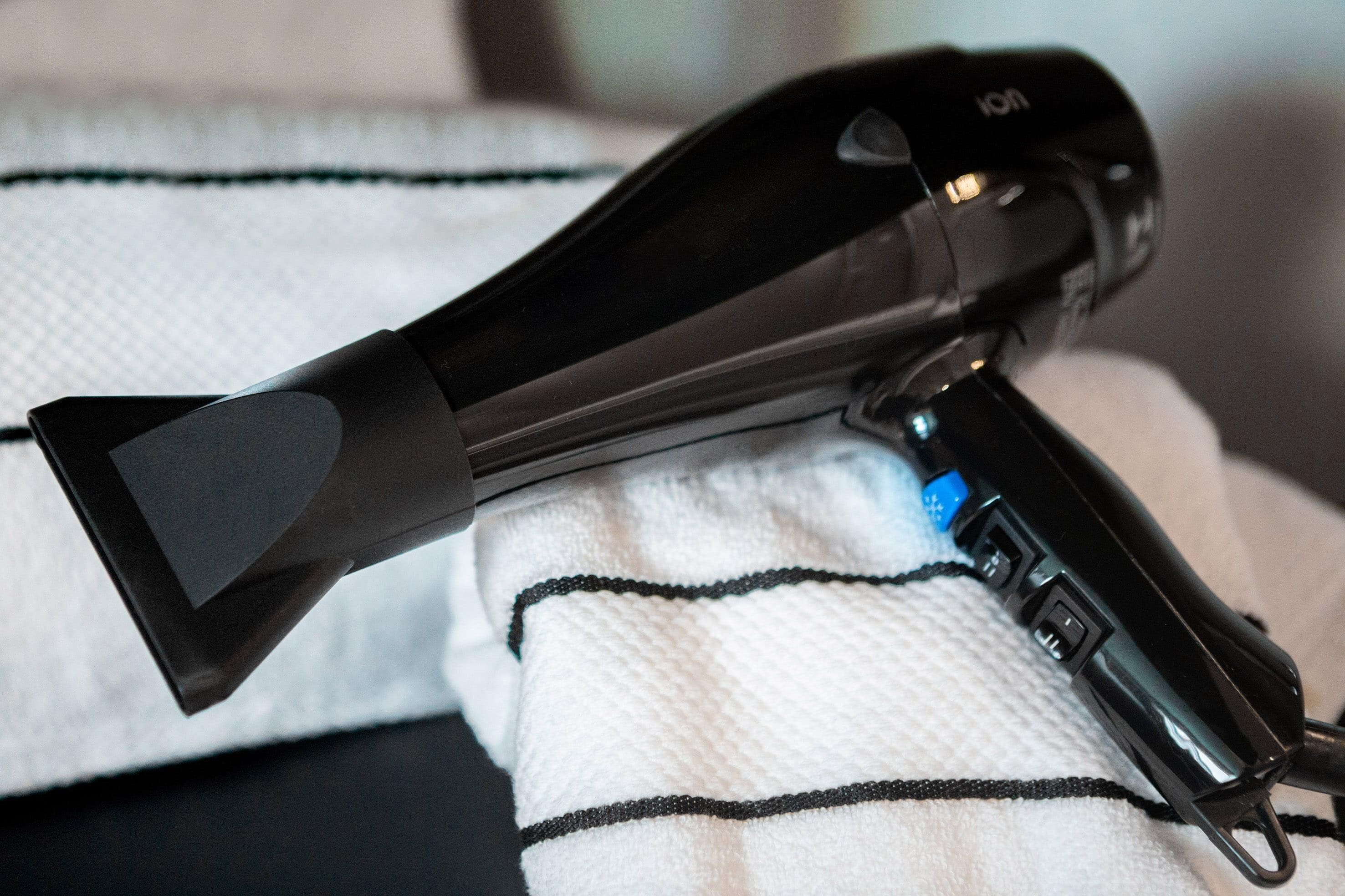 Un sèche-cheveux posé sur un lit recouvert d’une couverture à rayures noires et blanches.