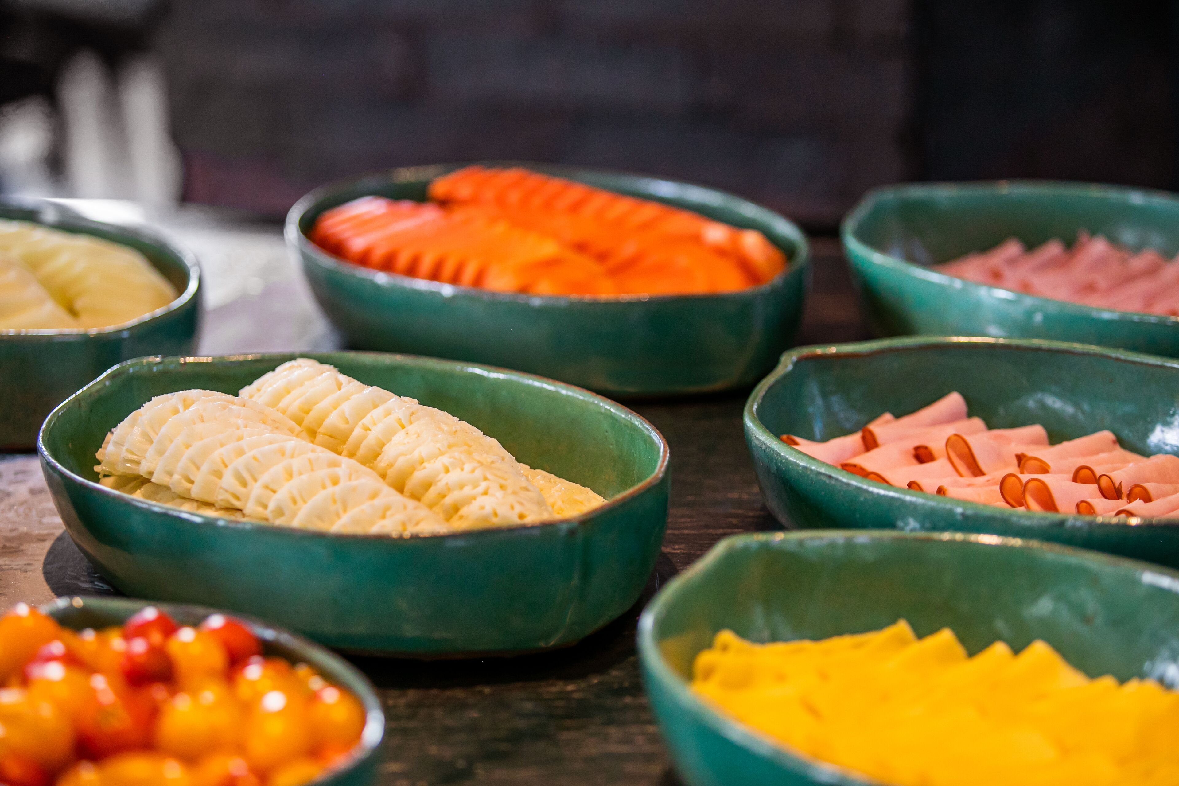 A variety of food items in green bowls on a wooden table.