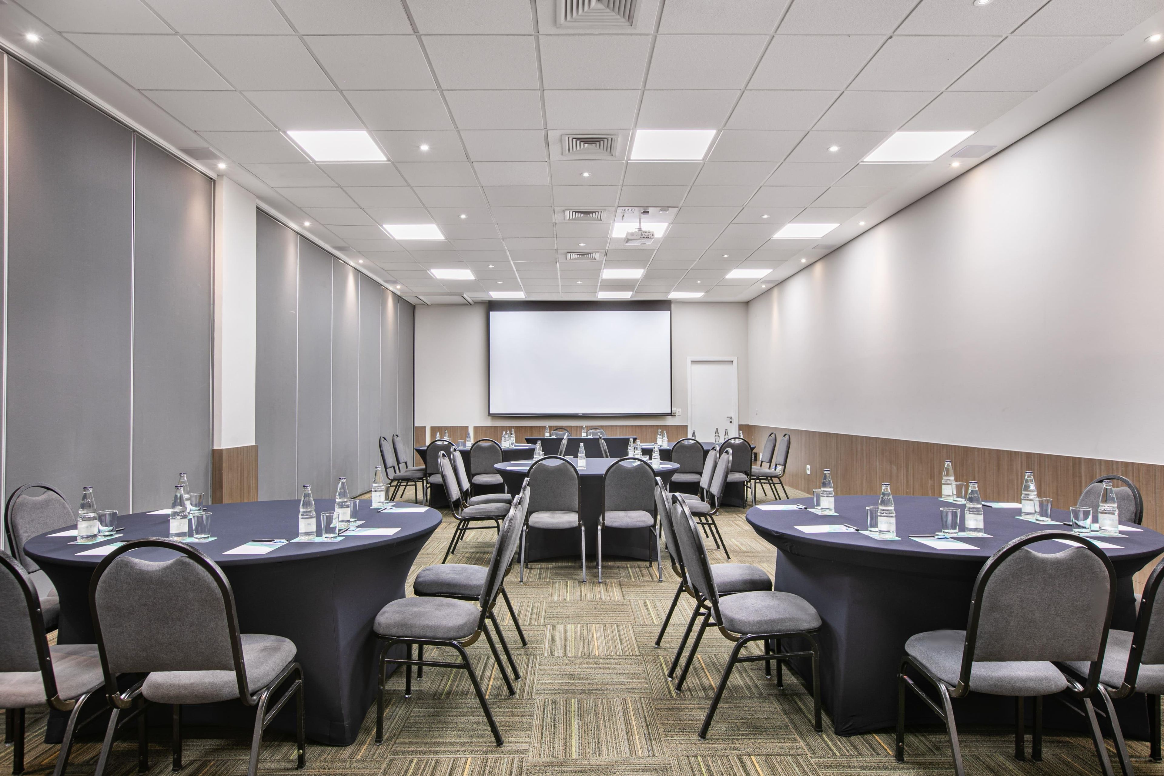 A conference room with round tables, chairs, and a projector screen.