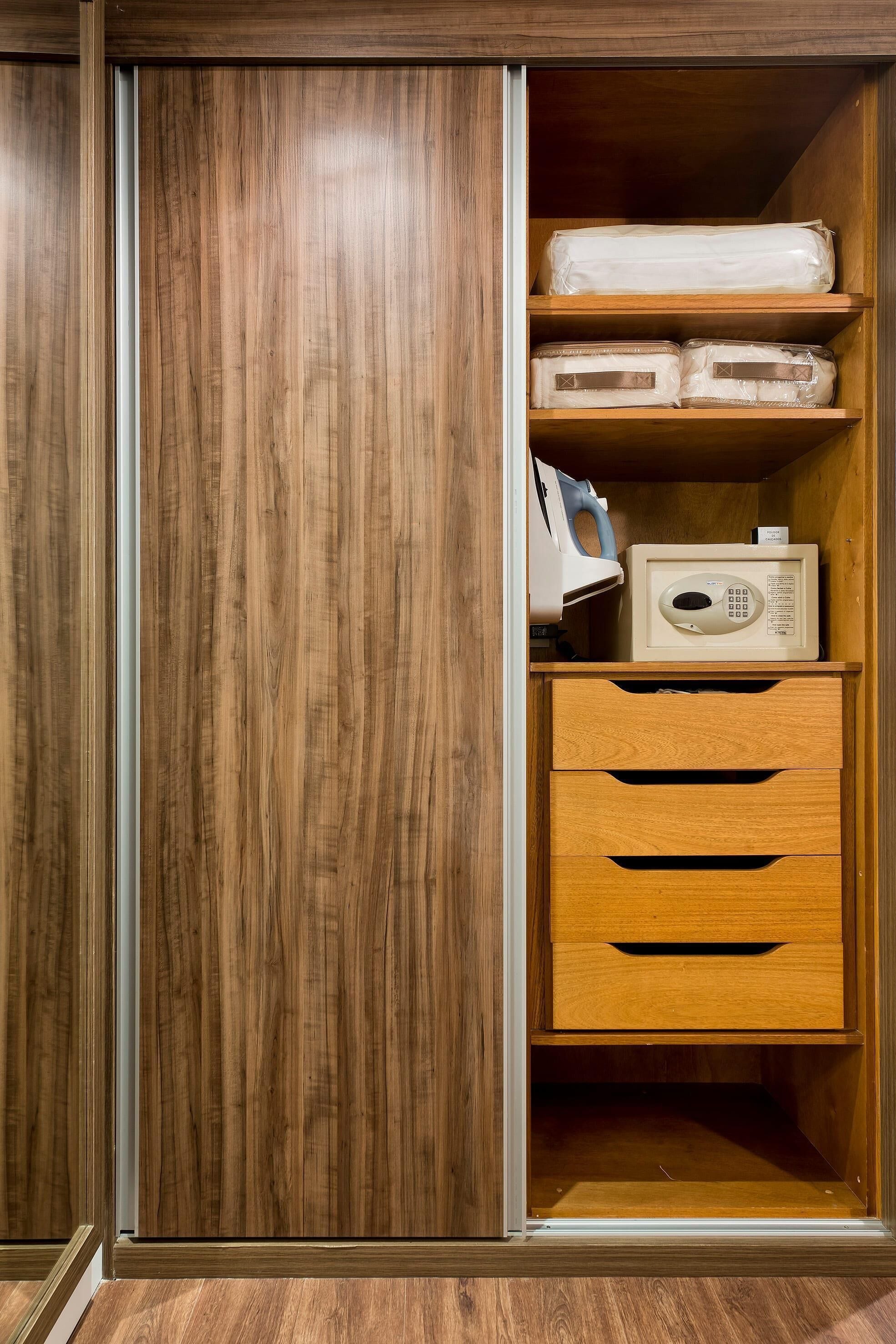A wooden wardrobe with a microwave and a coffee maker on the top shelf, and a drawer below.