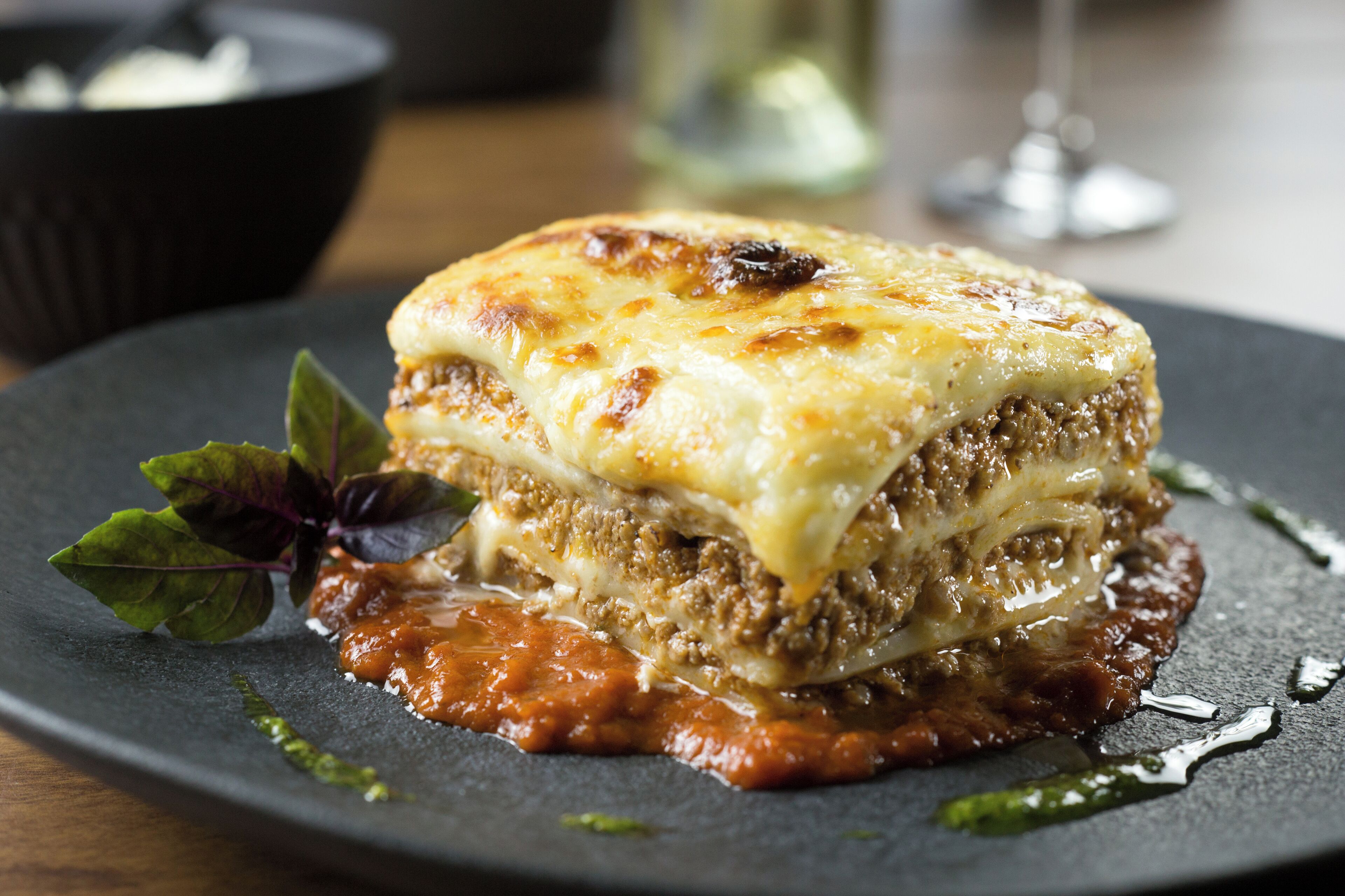 A dish of lasagna on a plate with a garnish of basil leaves.