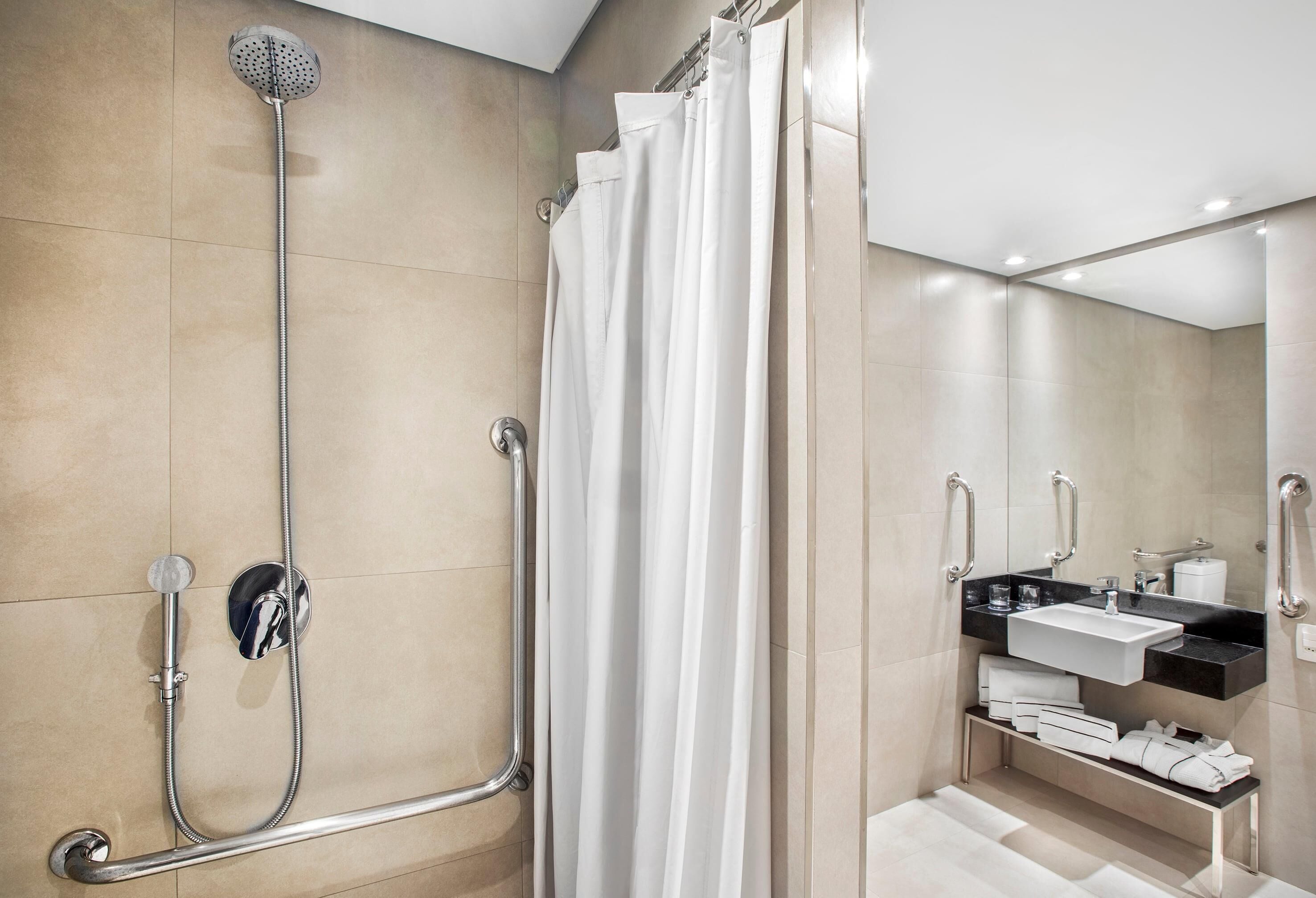 A modern bathroom with a walk-in shower, grab bars, a white sink, and a mirror.