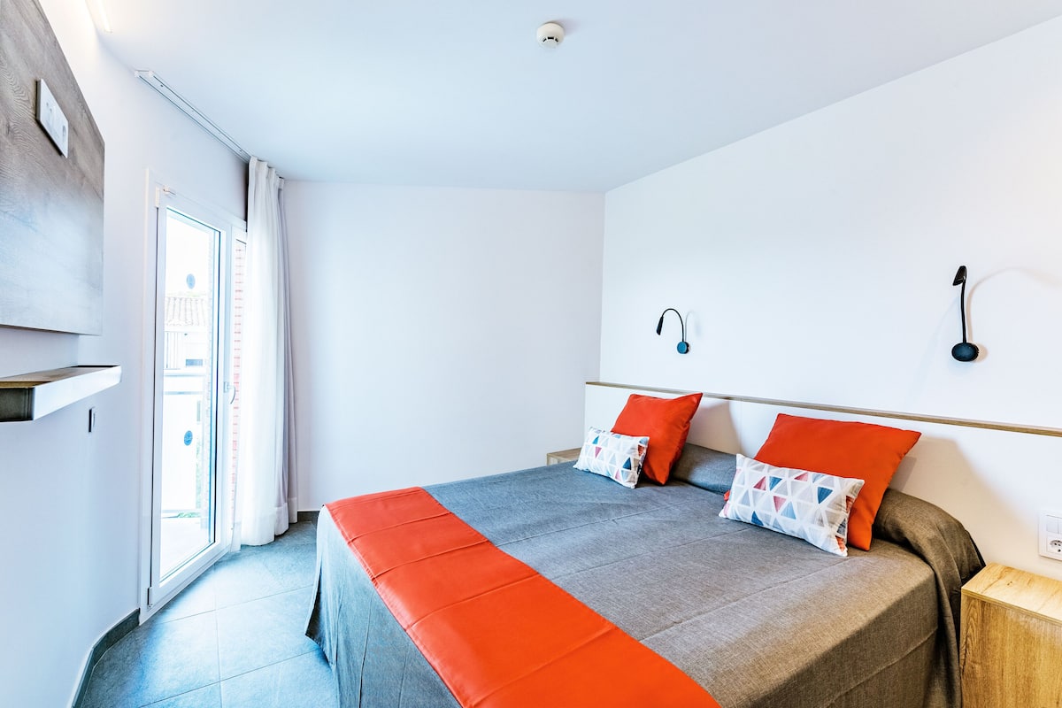 A modern bedroom with a large bed, two pillows, a bedside table, and a wall-mounted lamp.