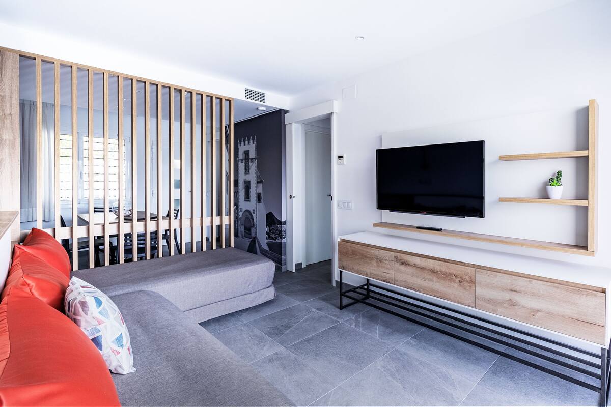 Una sala de estar moderna con un sofá gris, un mueble de televisión de madera y una escalera que lleva a otra habitación.