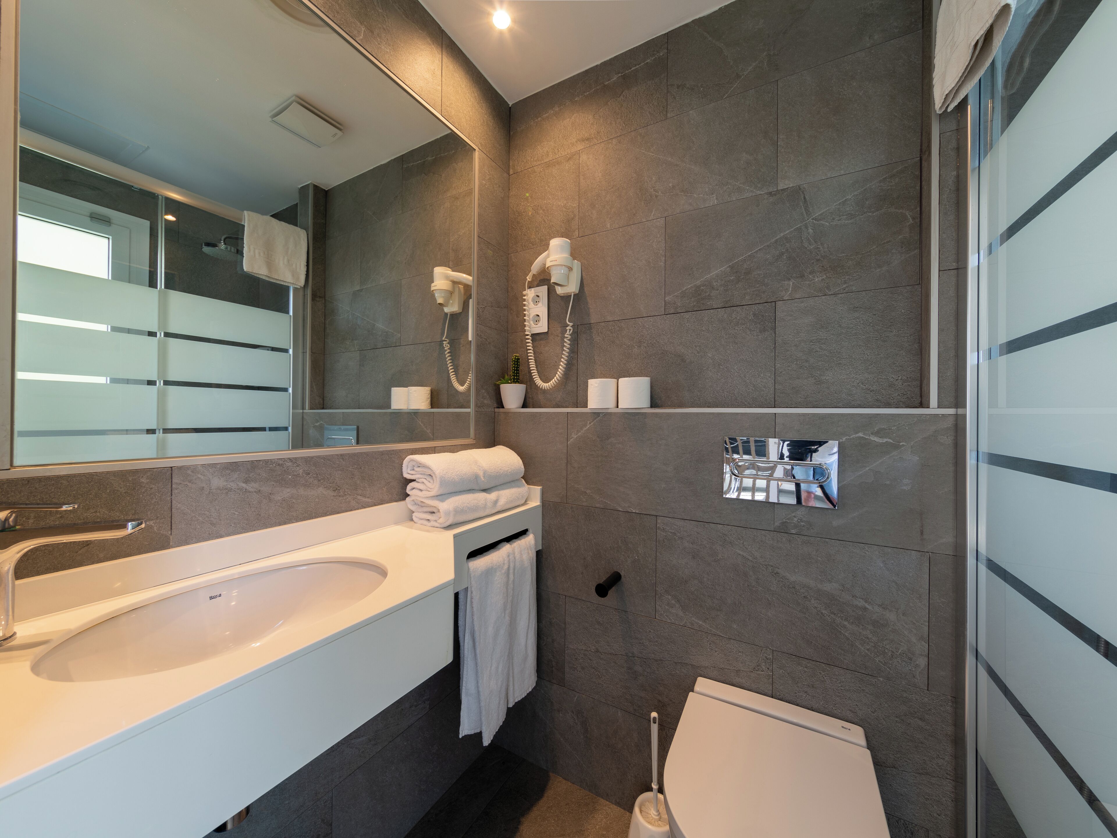 Un baño moderno con un espejo grande, un lavabo blanco, un inodoro y una zona de ducha.