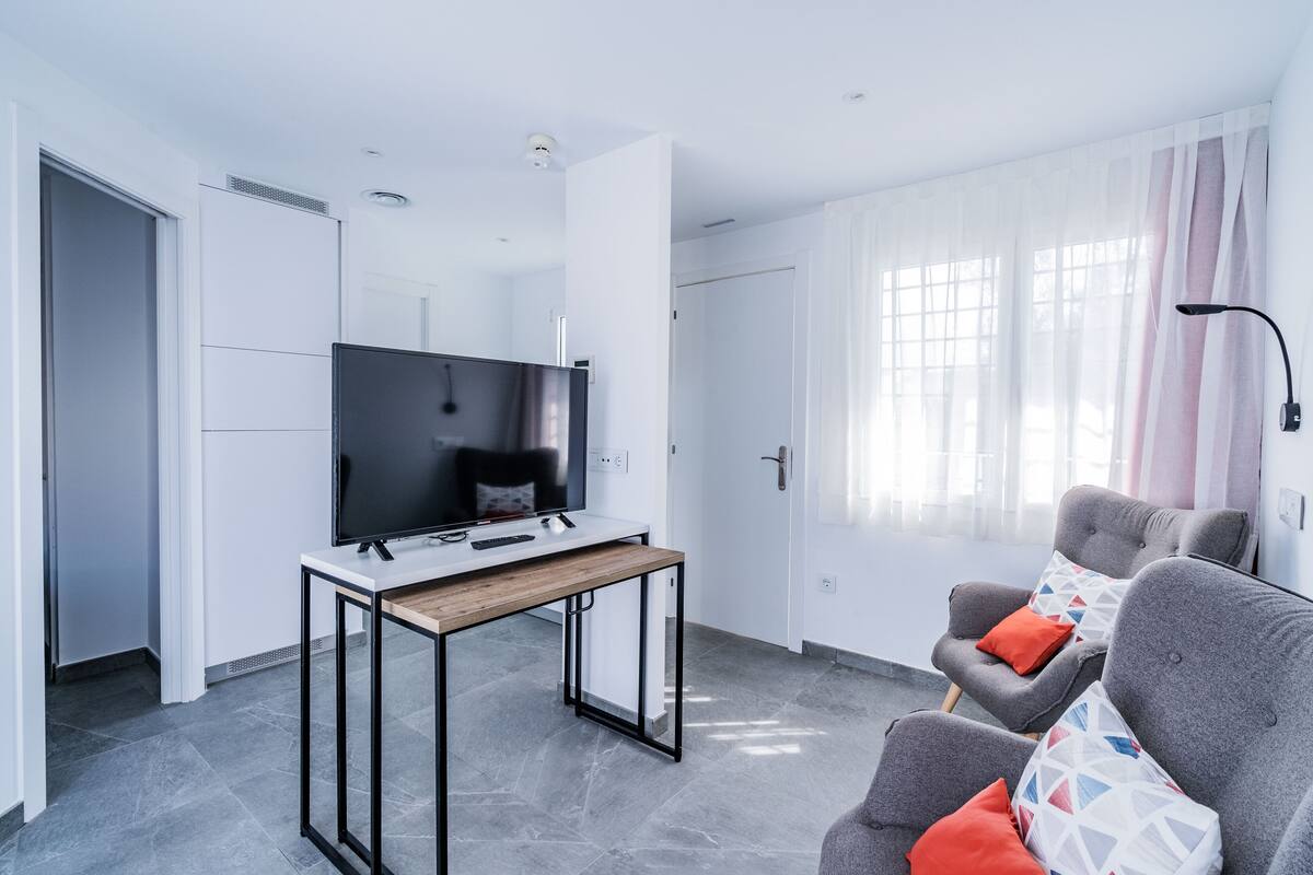 Una sala de estar moderna con un televisor de pantalla plana, una mesa de centro de madera y sillones grises con cojines estampados.