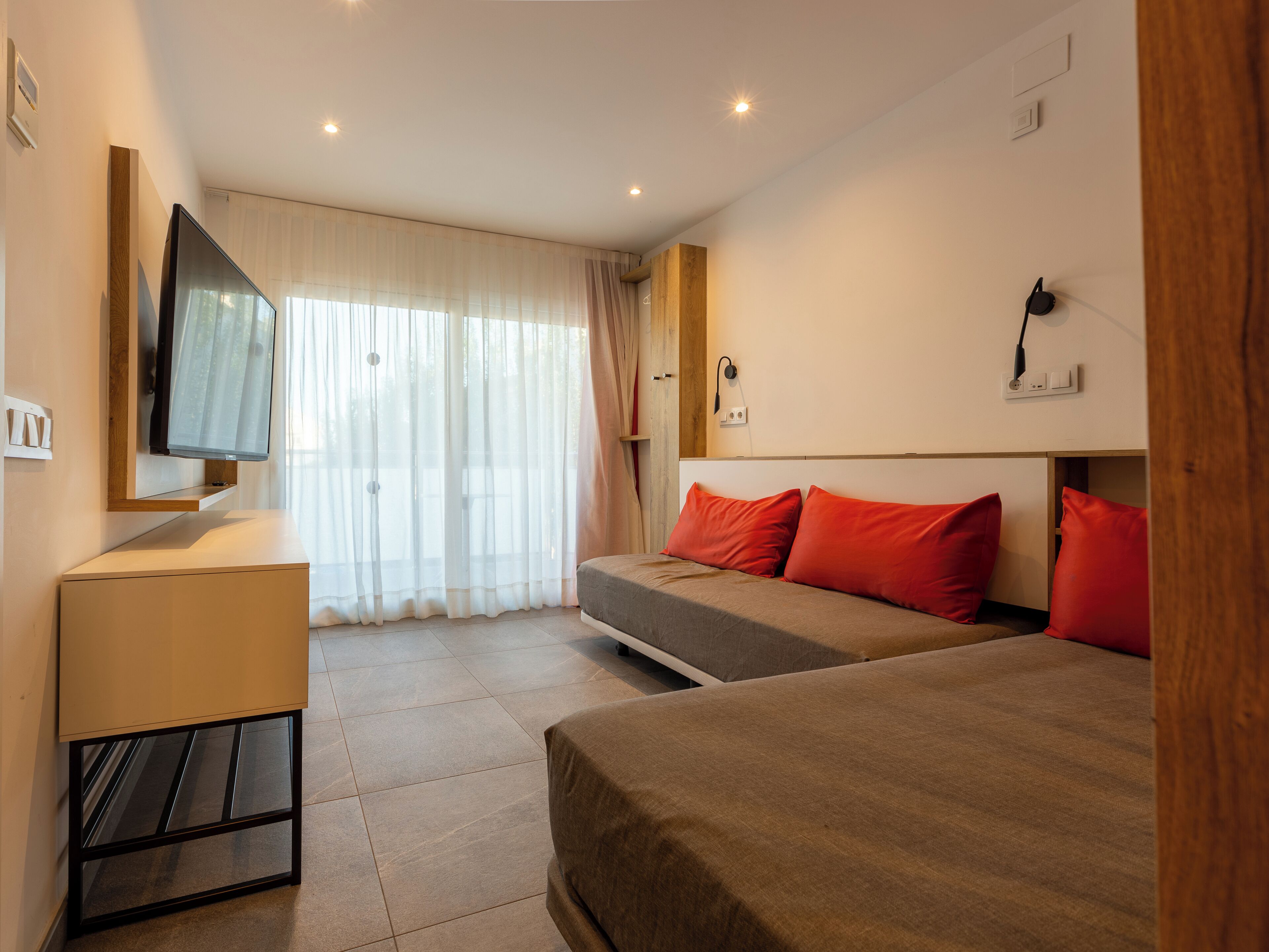 A hotel room with a bed, a desk, a TV, and a window with curtains.