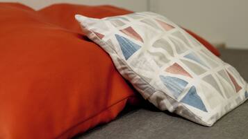 A bed with a grey mattress and two pillows, one orange and one with a geometric pattern.