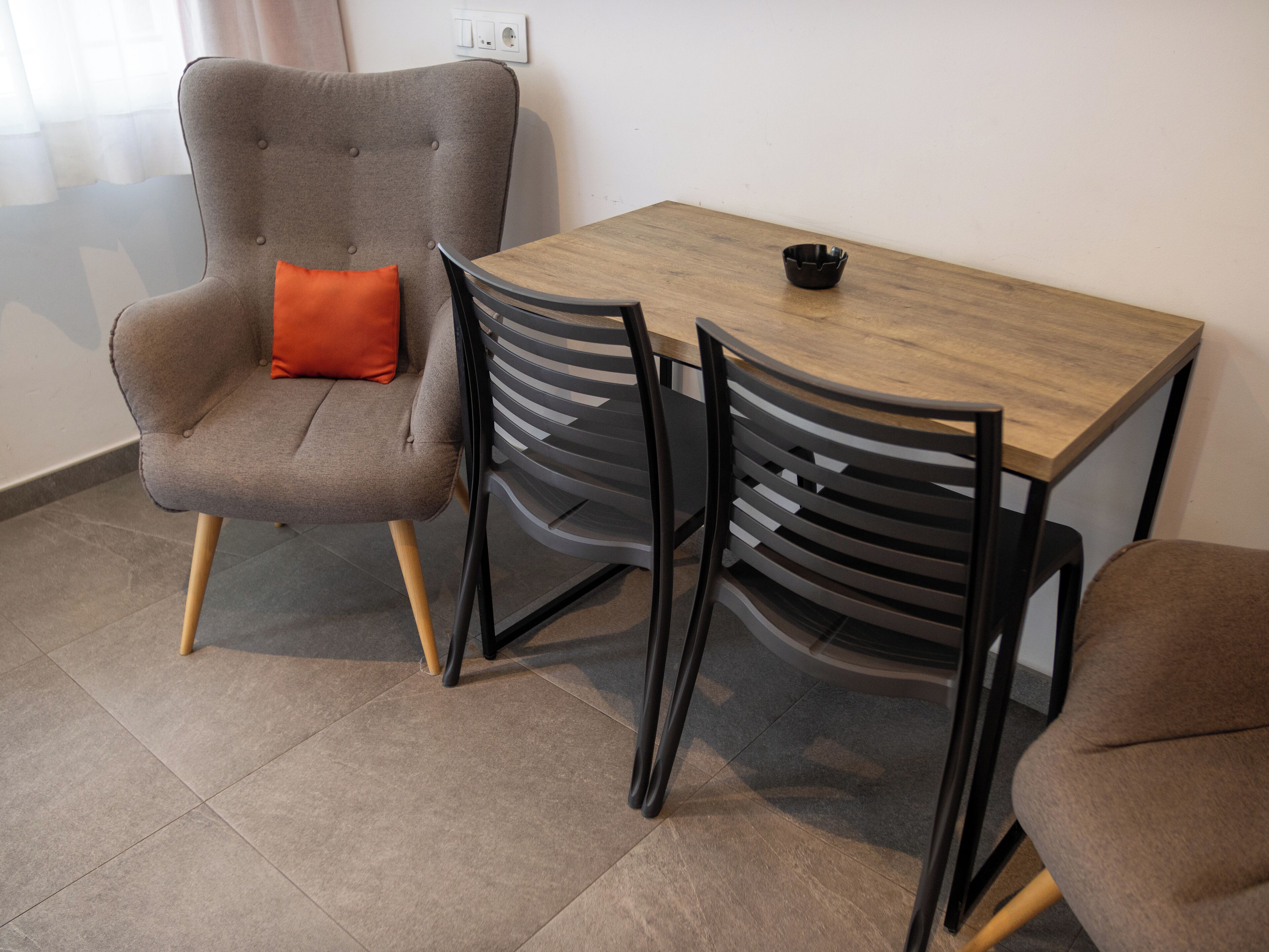 A dining area with a grey upholstered chair, a wooden table, and black chairs with a unique design.