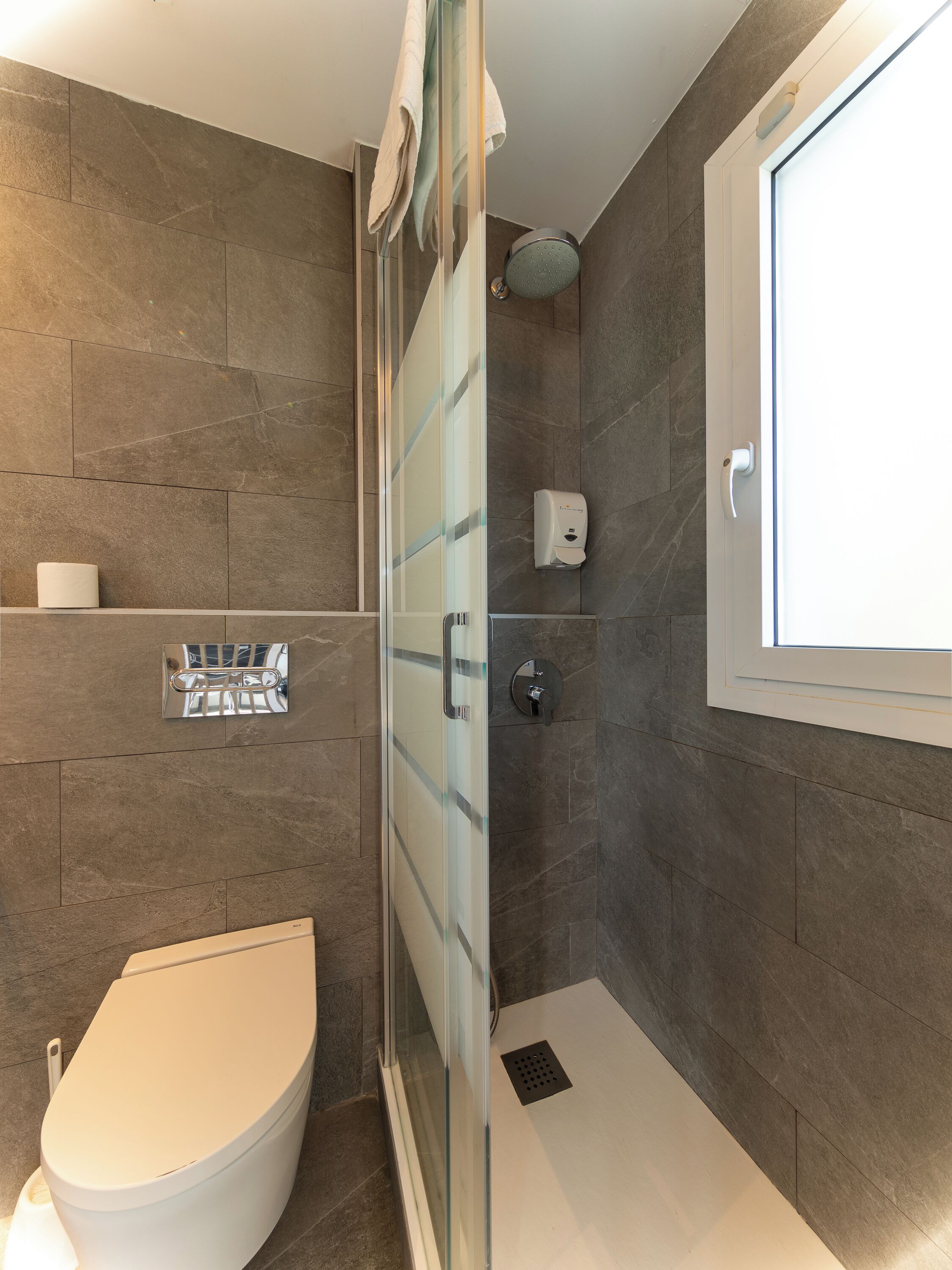 A modern bathroom with a glass shower enclosure, a toilet, and a hand soap dispenser.