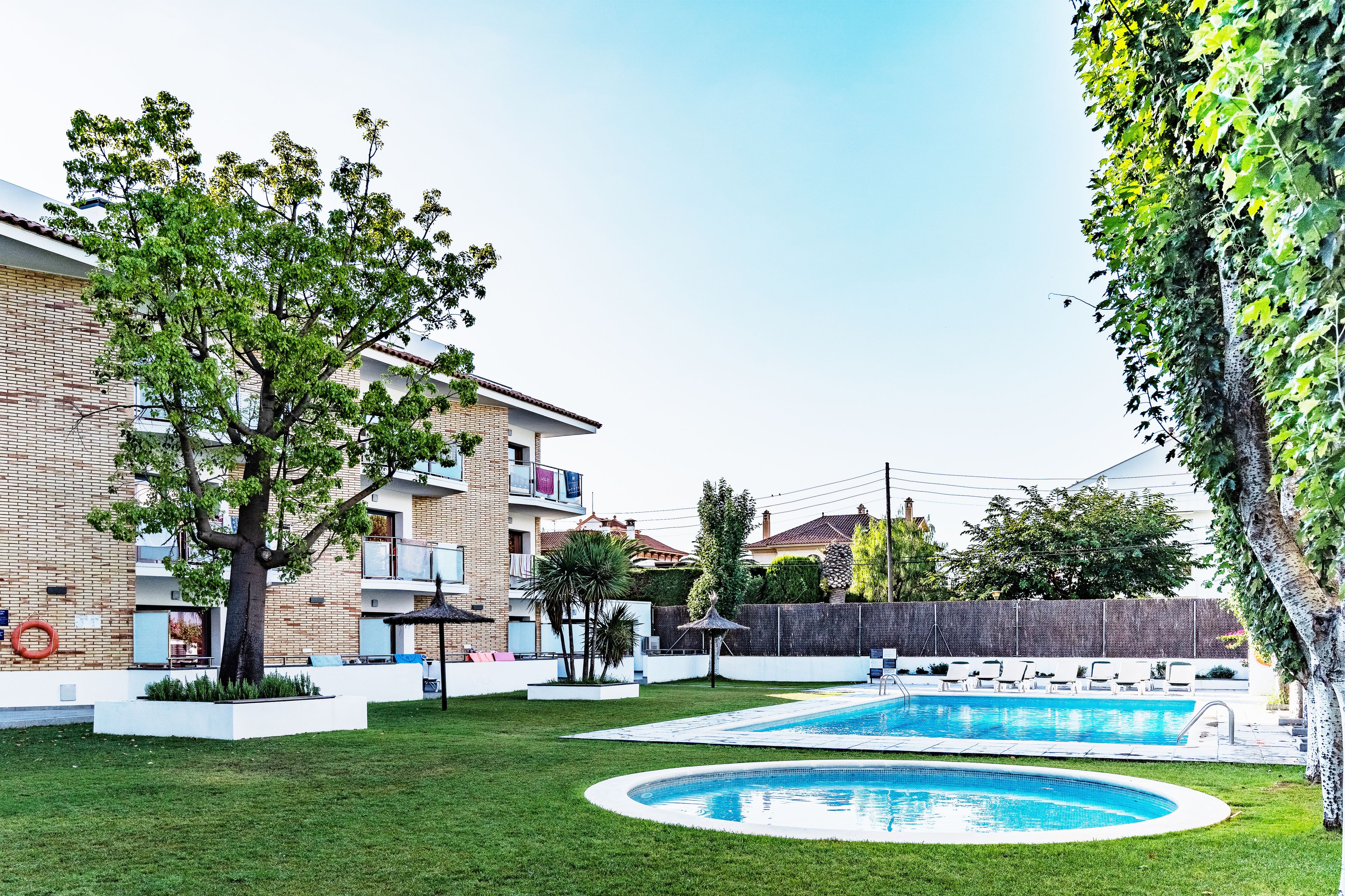 Un barrio residencial con piscina, césped cuidado y un edificio de ladrillo con balcones.