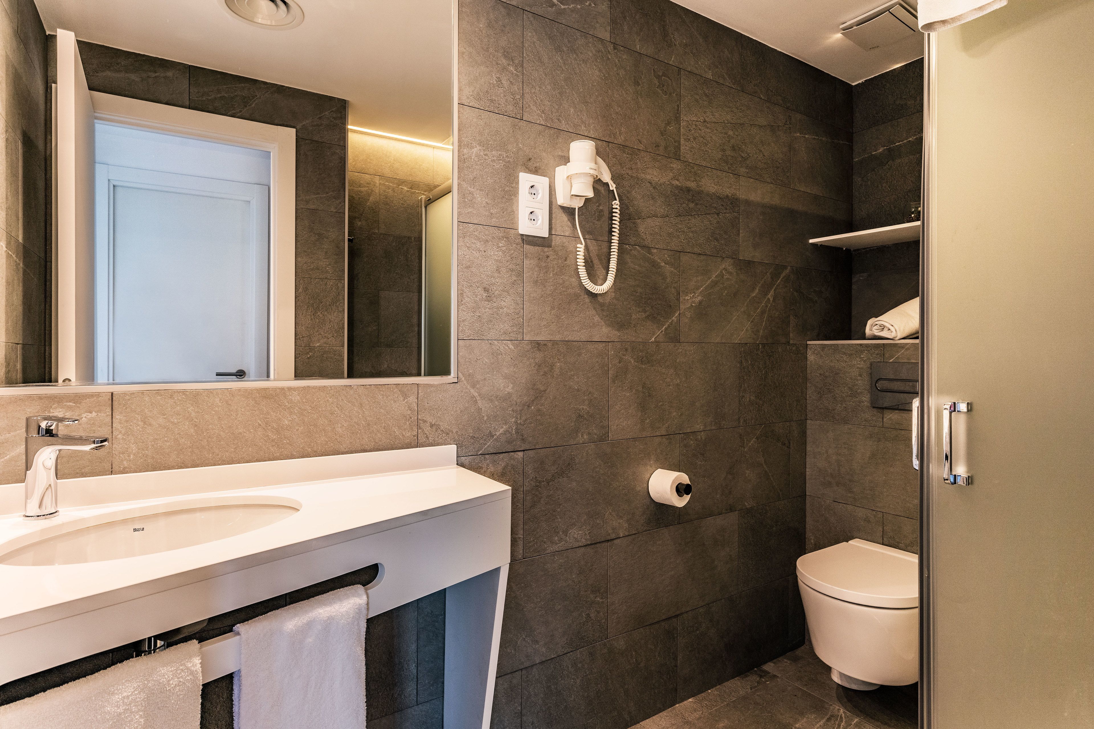 Een moderne badkamer met een witte wastafel, toilet en douche.