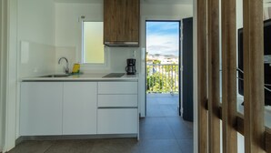 A modern kitchen with white cabinets, a stainless steel sink, and a coffee maker. There is a window with a view of buildings and a balcony.