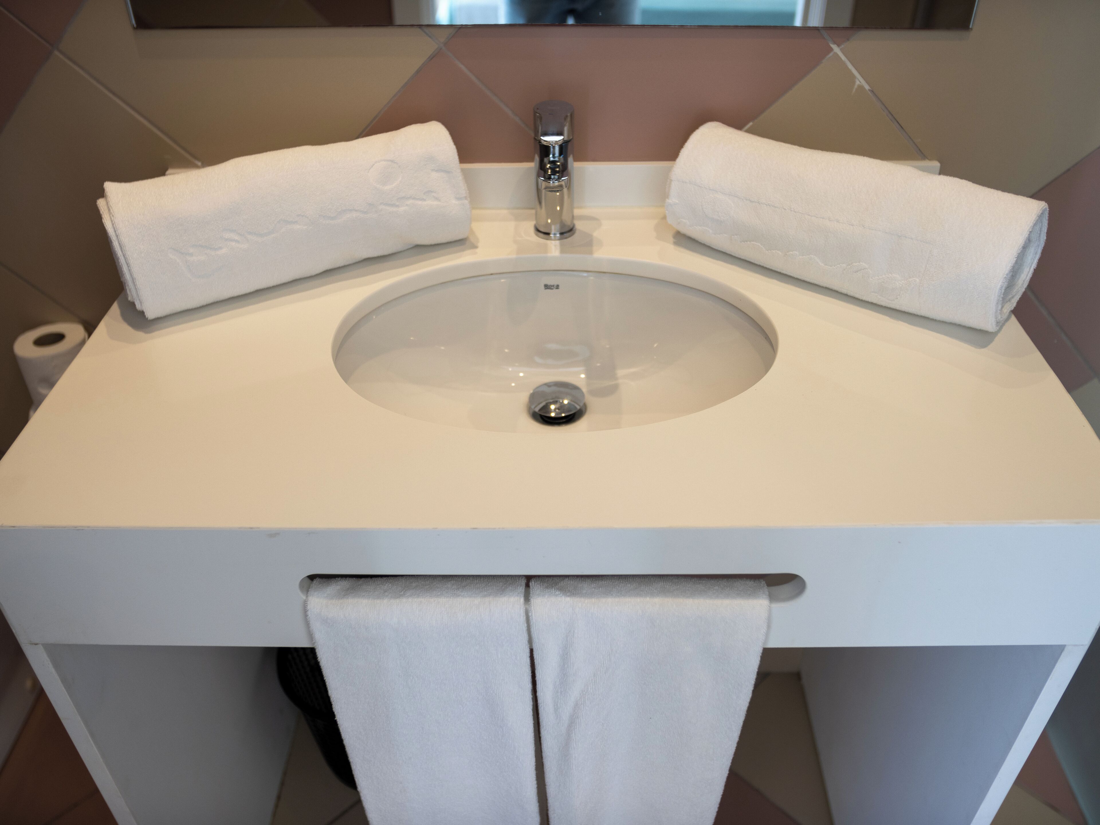 Un bany amb un lavabo blanc, dues tovelles i un roule de paper higiènic.