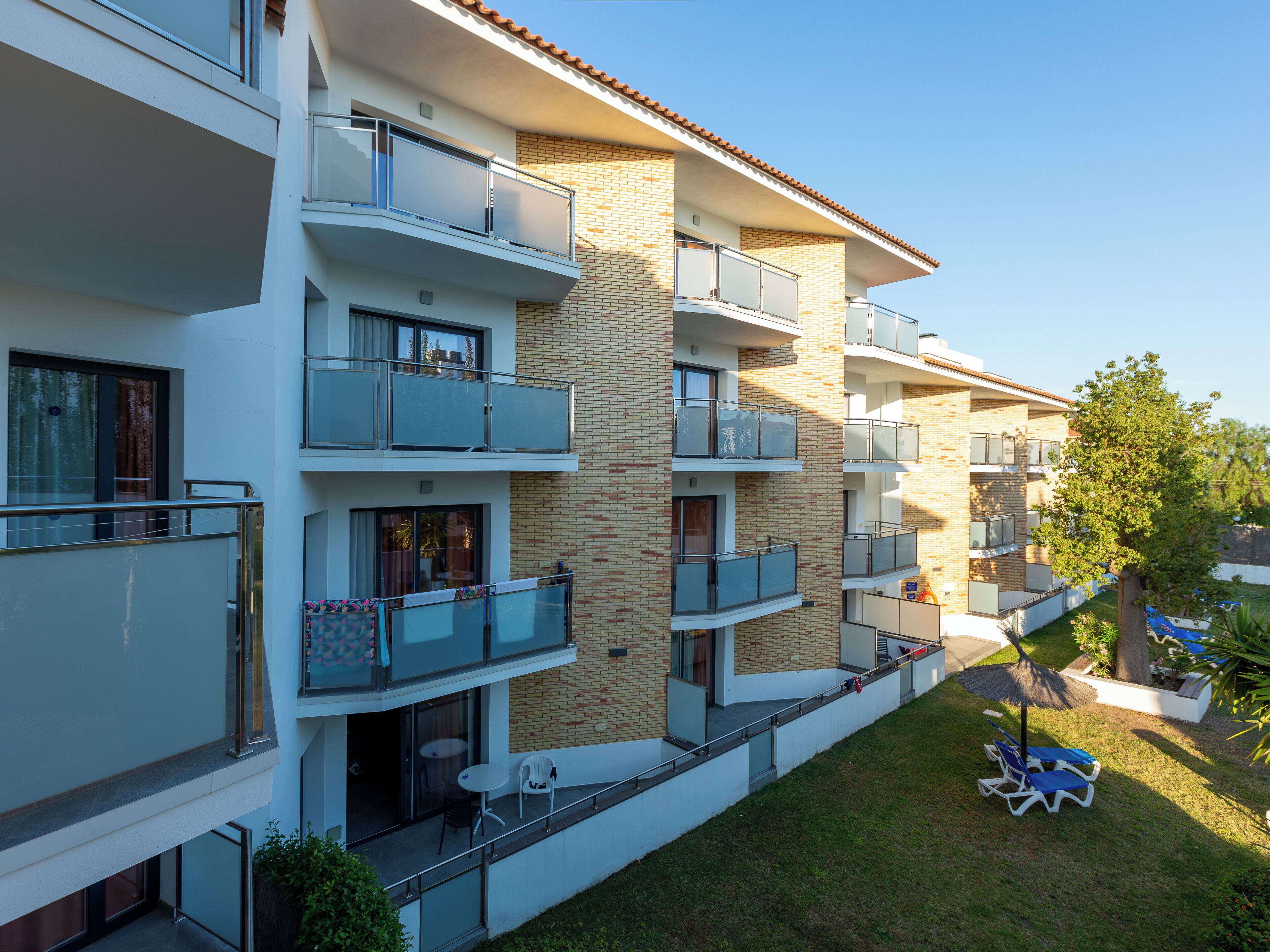 Un hotel de varios pisos con balcones, un pequeño espacio de estar al aire libre y un césped bien cuidado.