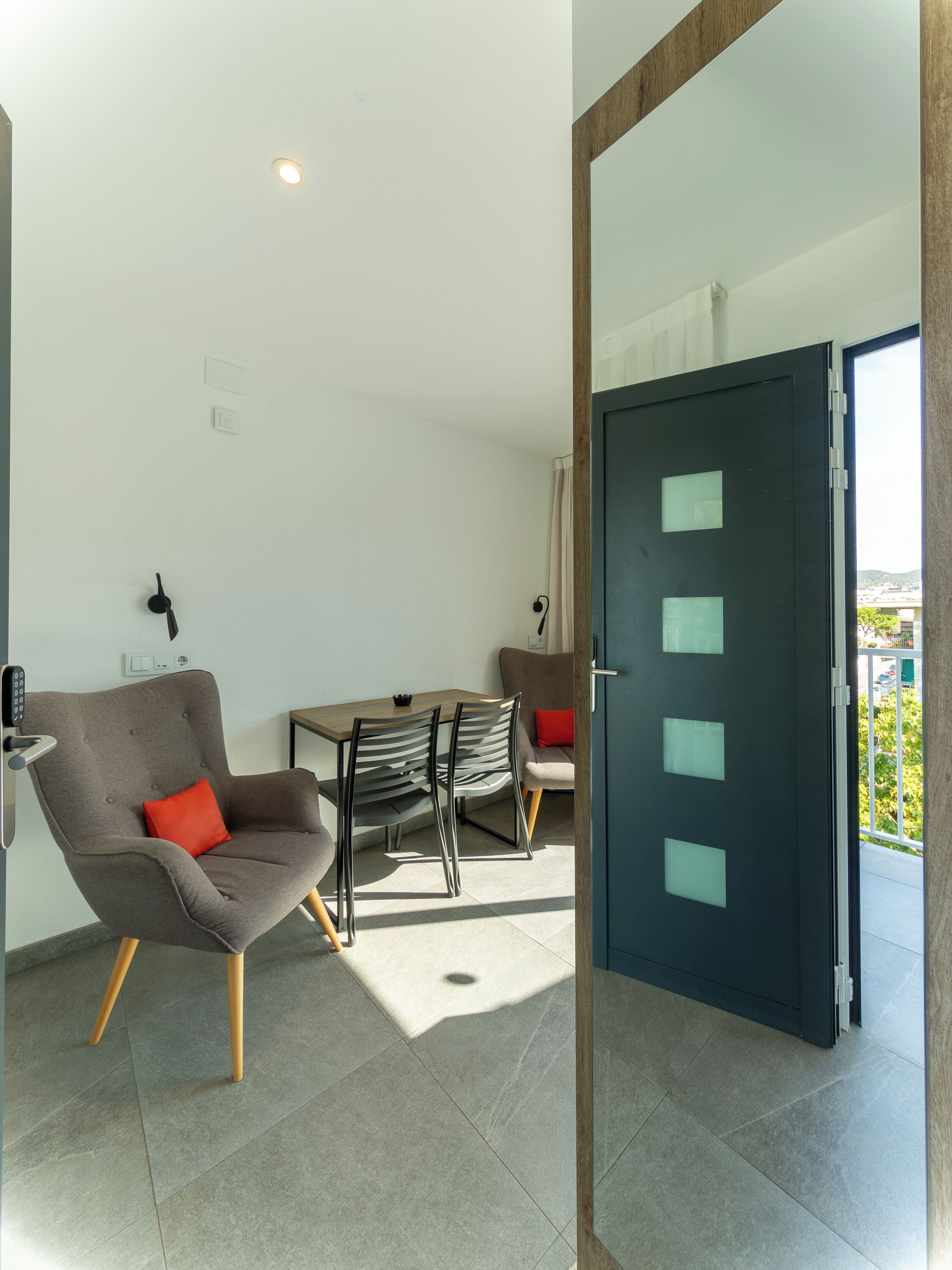 A modern room with a dining table, two chairs, a sofa, and a door leading to an outdoor balcony.