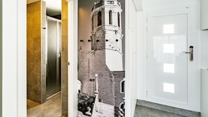 A hallway with a modern elevator, a door with a glass panel, and a mural of a historical tower.