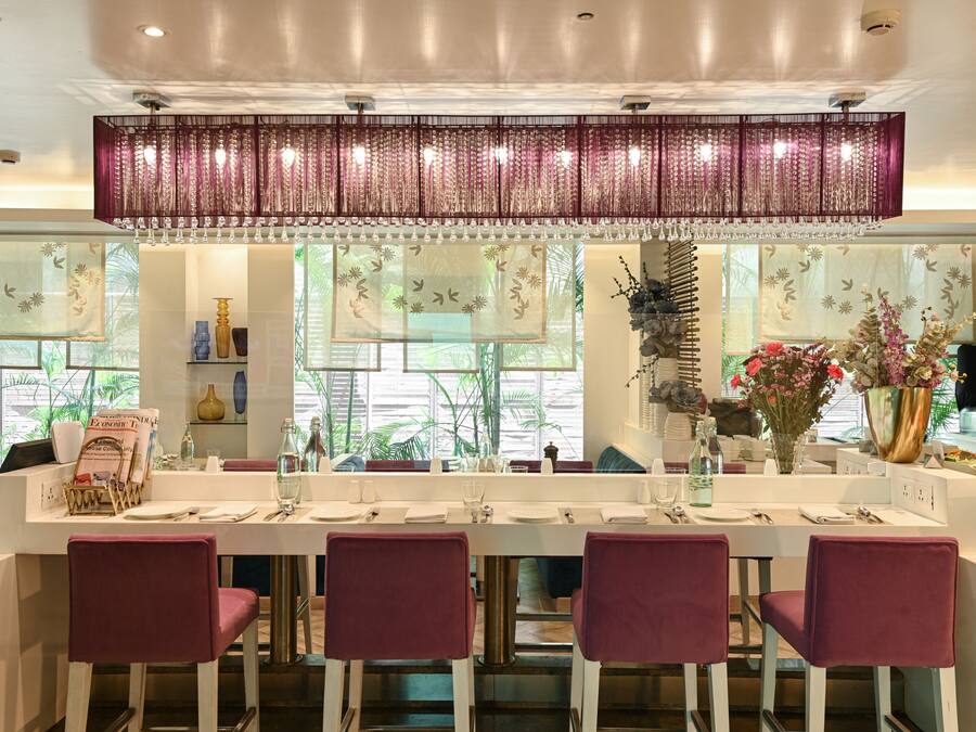 A modern dining area with a long table, four chairs, and a decorative hanging light fixture.