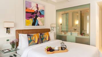 Una habitación de hotel con cama, mesita de noche y una bandeja con frutas y una cafetera.