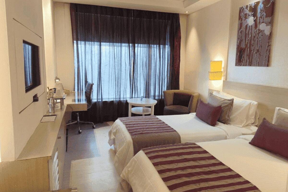 Habitación de hotel con dos camas, un escritorio, una silla, una mesita, un televisor y una ventana con cortinas.