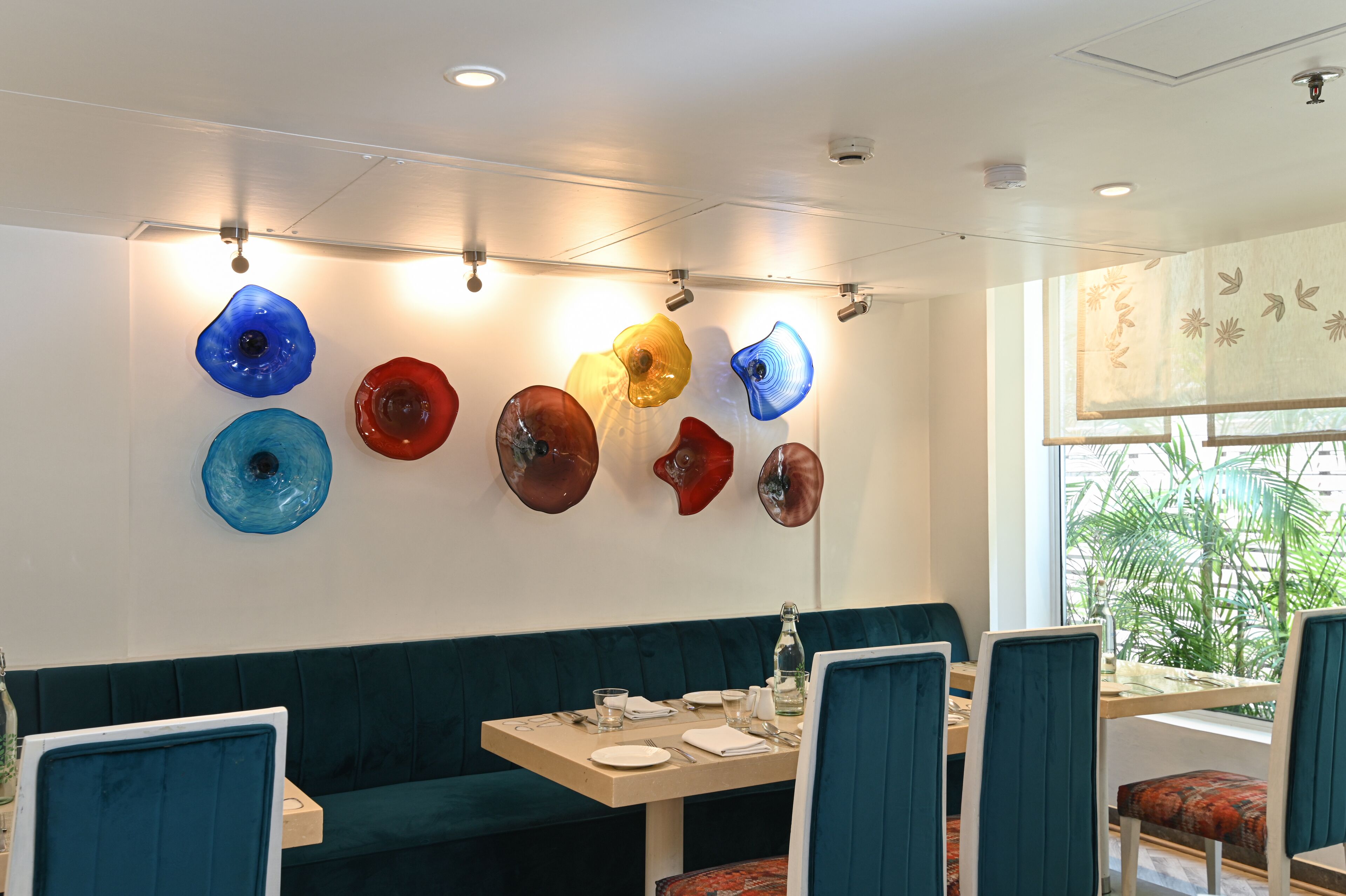 A restaurant interior with a green booth seating area, a wooden table with white plates, and colorful glass art on the wall.