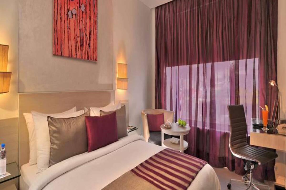 Una habitación de hotel con cama, escritorio, silla y un ventanal con cortinas.