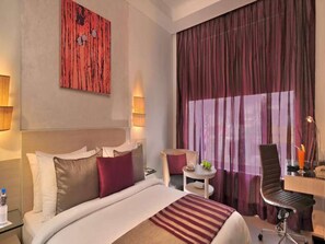 A hotel room with a bed, a desk, a chair, and a large window with curtains. - The Ashtan Sarovar Portico Delhi (New Delhi)
