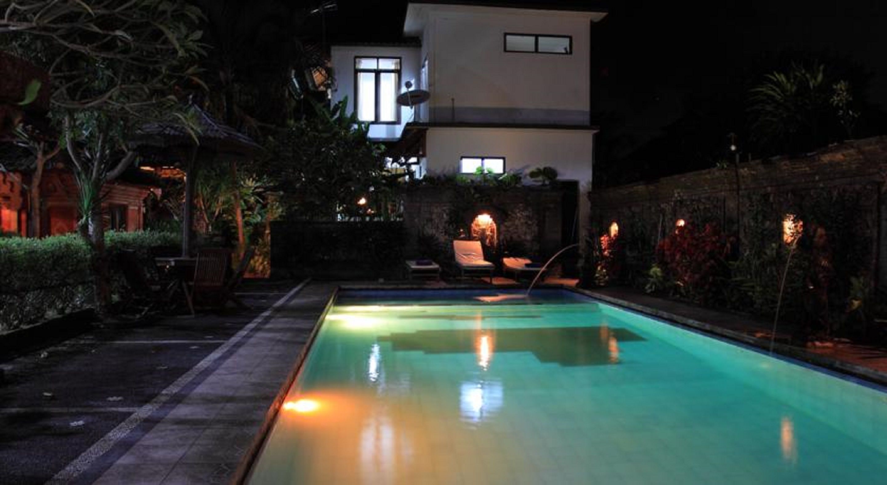 A nighttime swimming pool with lounge chairs and a building in the background.
